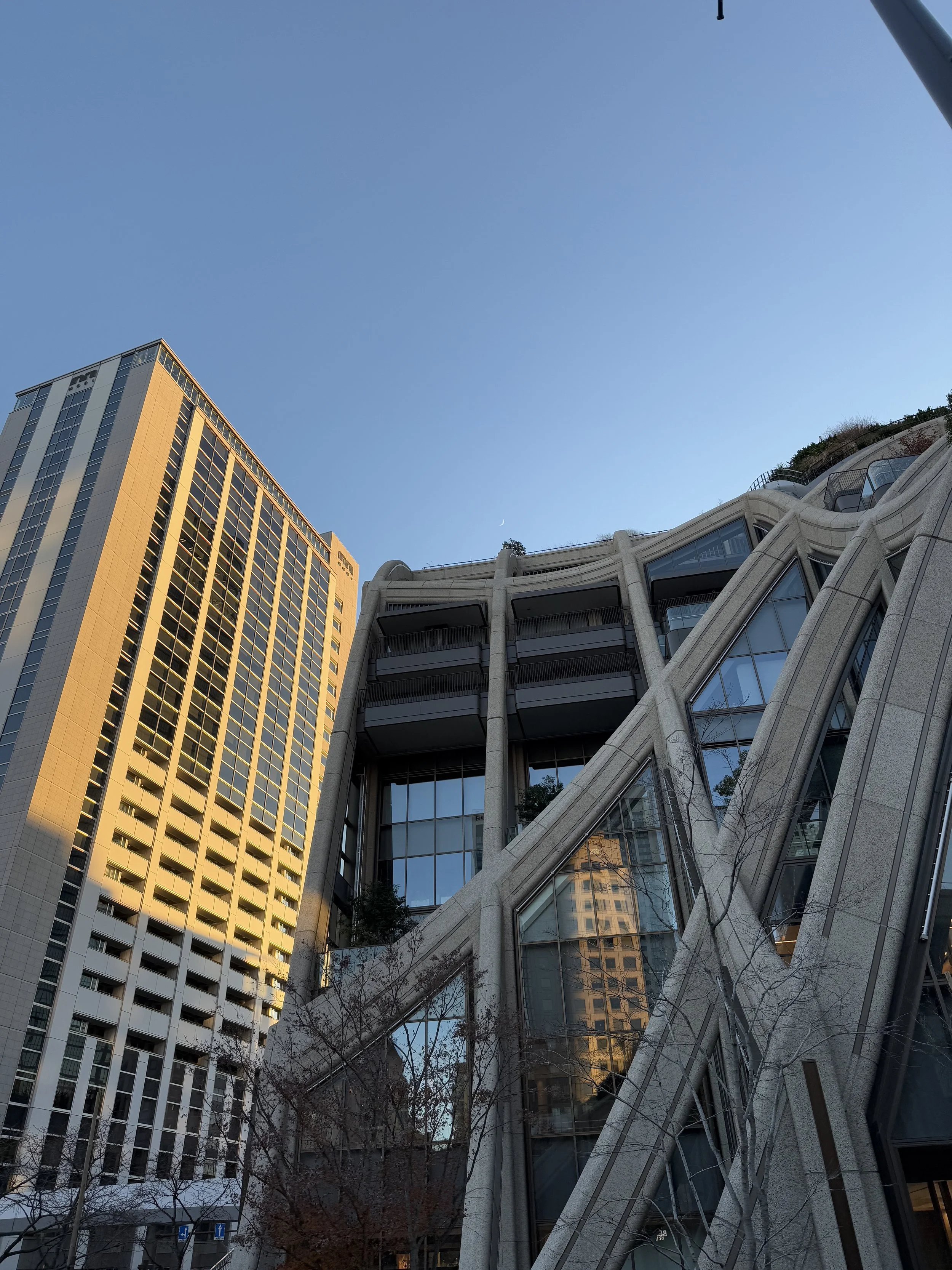 Contemporary urban architecture in Tokyo with intersecting glass and concrete structures reflecting nearby buildings