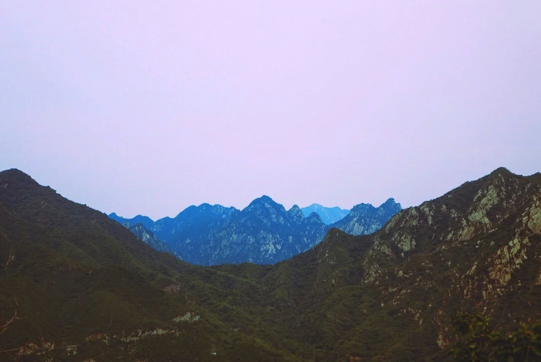 Mountain range with rugged peaks and green slopes under a light purple sky.