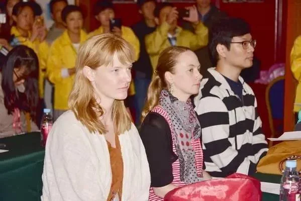 People attending a presentation or event, sitting at tables with some taking photos or videos.