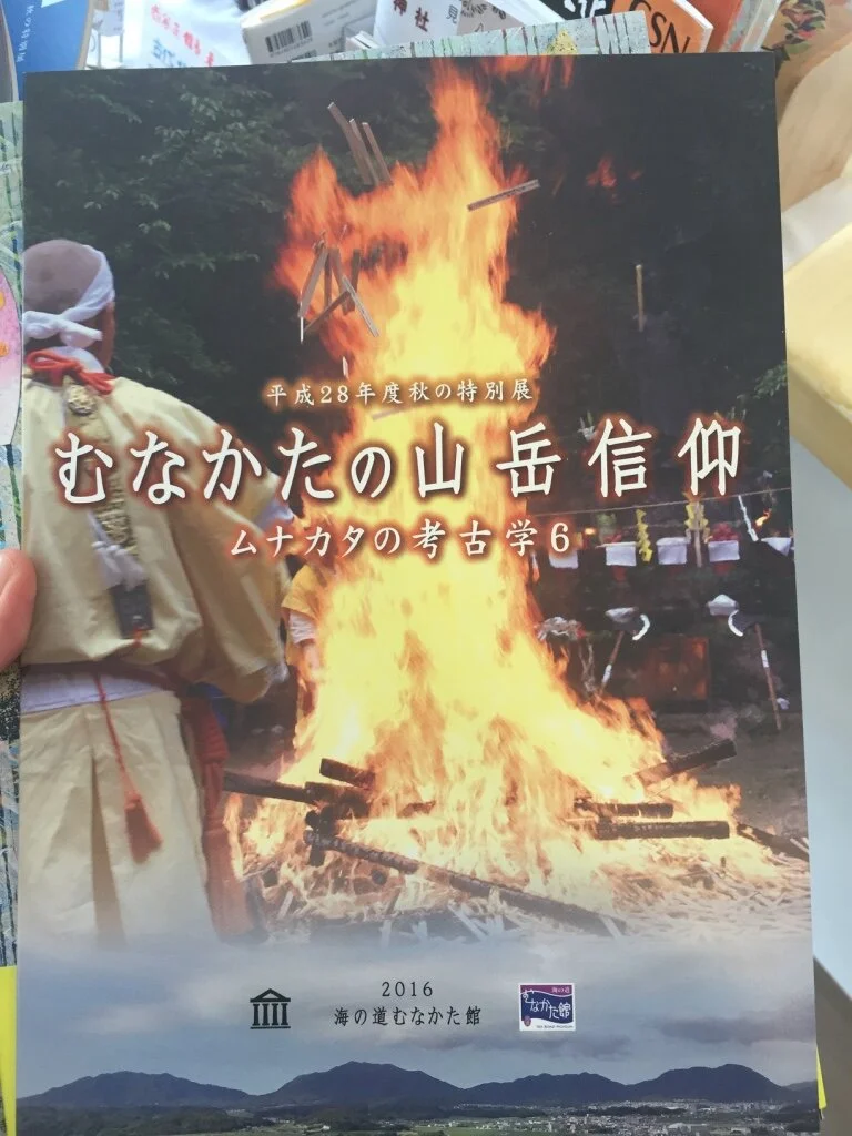 A Japanese brochure featuring a large outdoor fire with flames and smoke, with people dressed in traditional clothing nearby, set against a background of trees and mountains.