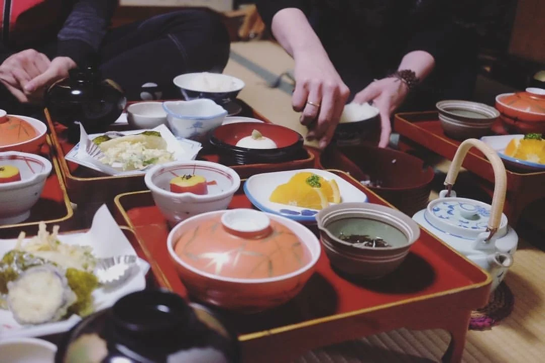 Traditional Japanese meal set with various small dishes, bowls, and a teapot on a wooden table.