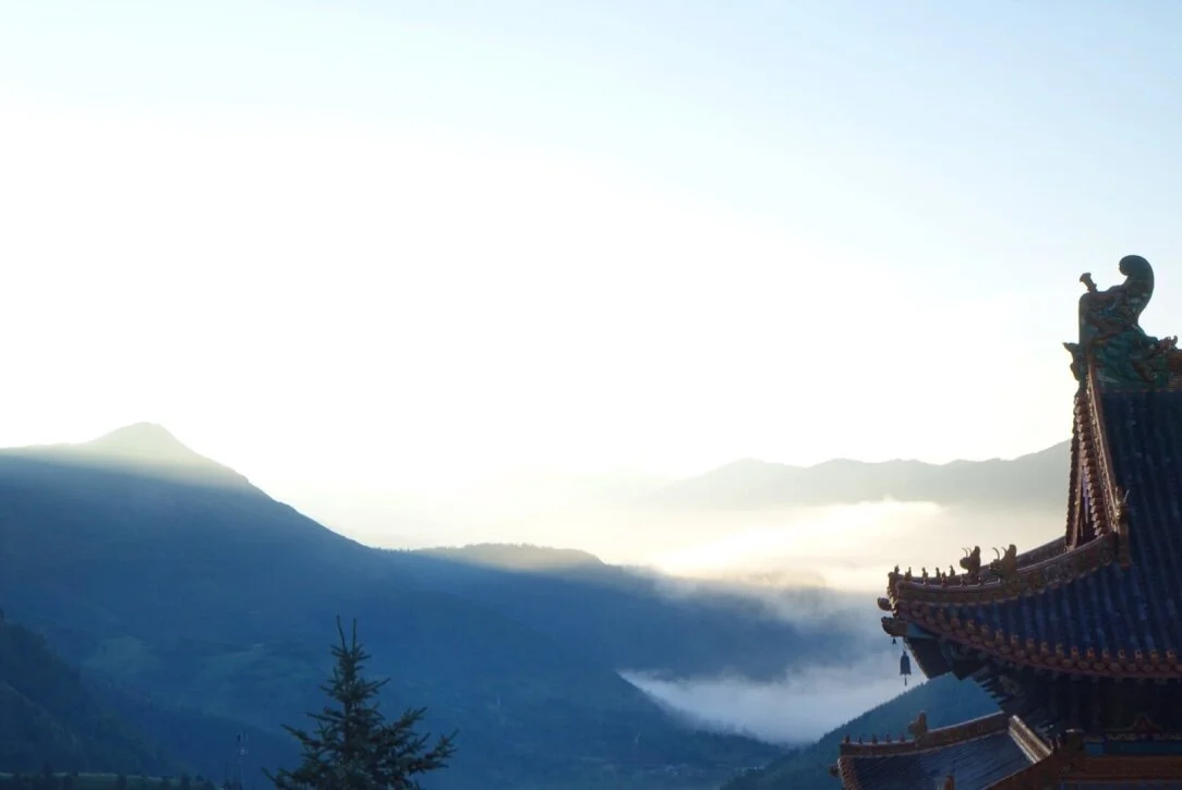 View of mountains and sky with the corner of a traditional Asian temple roof in the foreground.