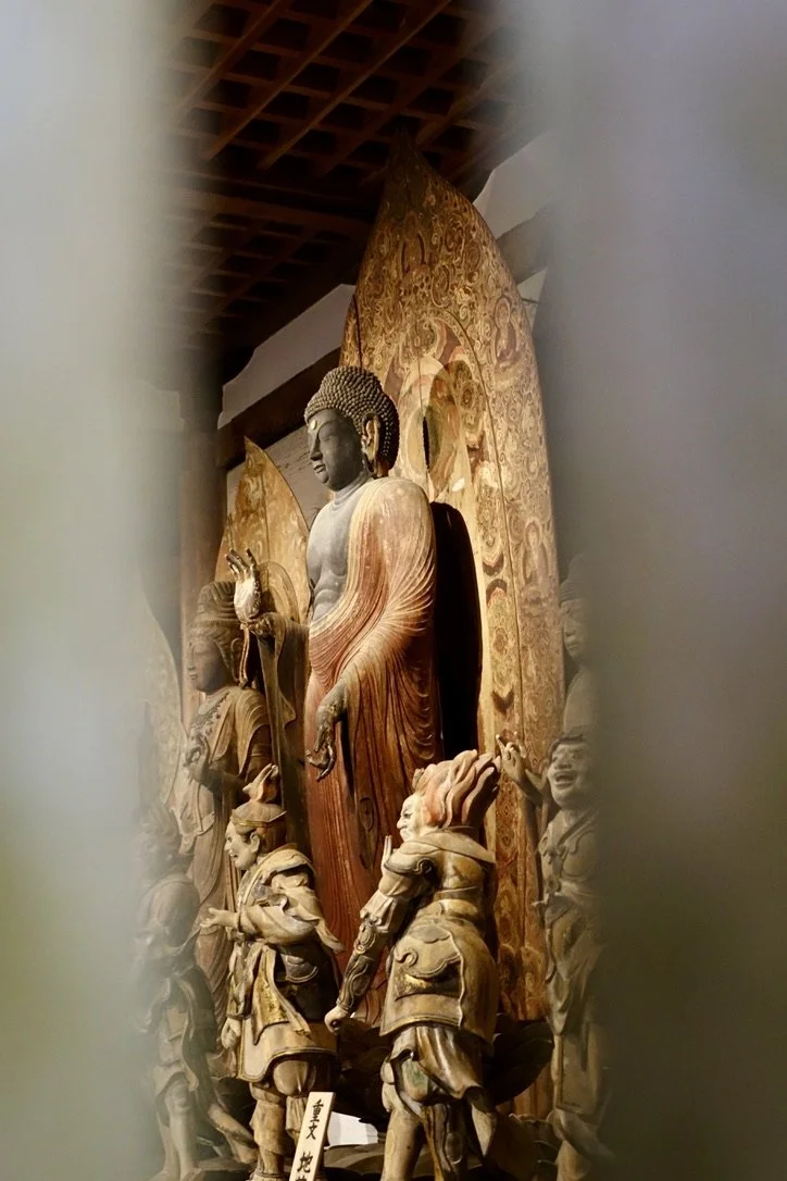 Buddha statues and wooden sculptures inside a temple, framed by blurred foreground elements.
