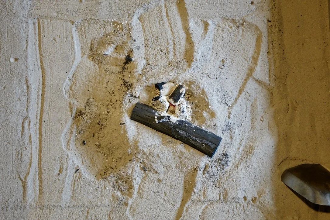 A small fire in a sand pit, with burning wood and ashes, near the corner of a tiled floor.
