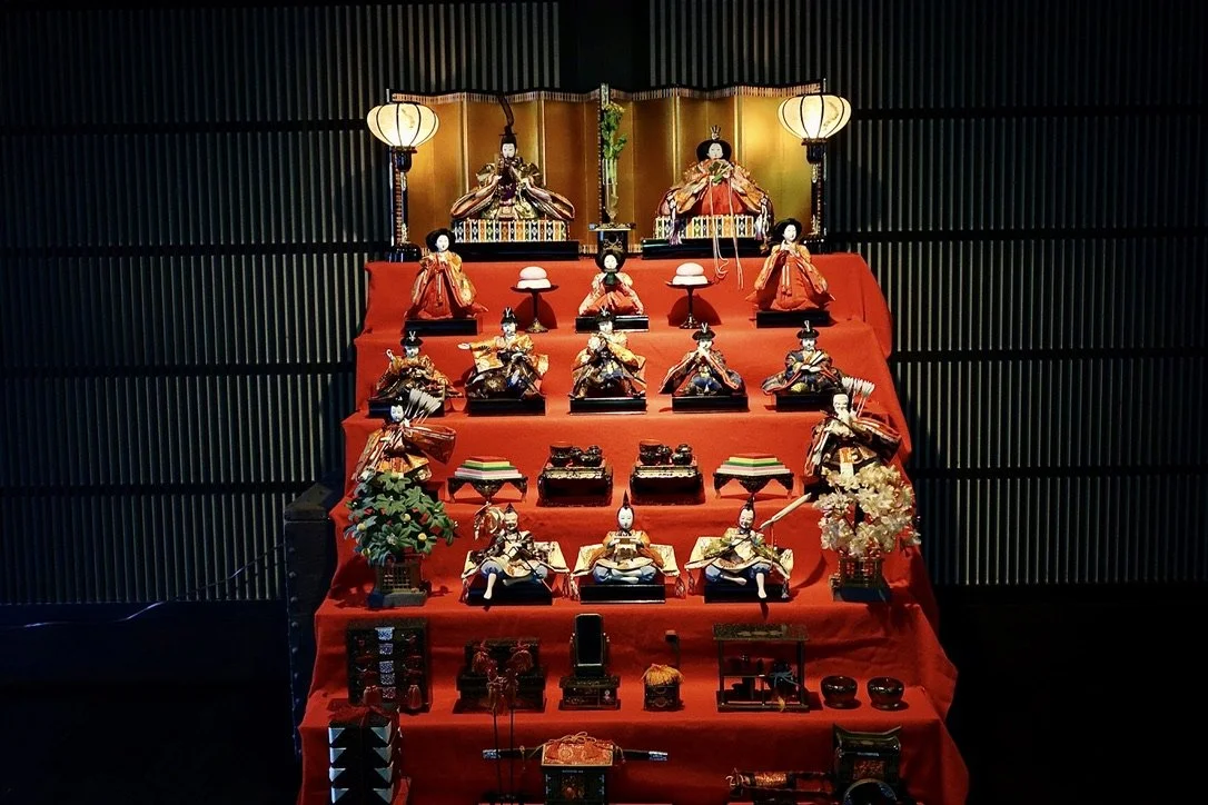 Traditional Japanese Hina doll display with multiple dolls dressed in colorful kimonos on a red tiered platform.