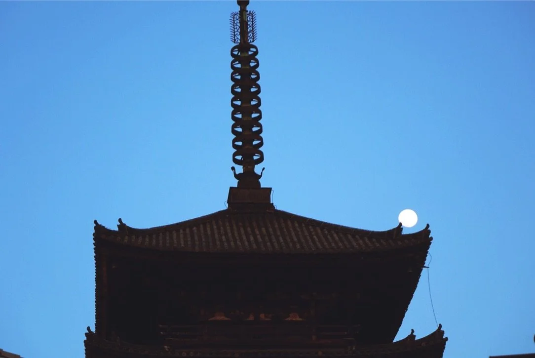 Nighttime image of a pagoda roof with a full moon in the background.