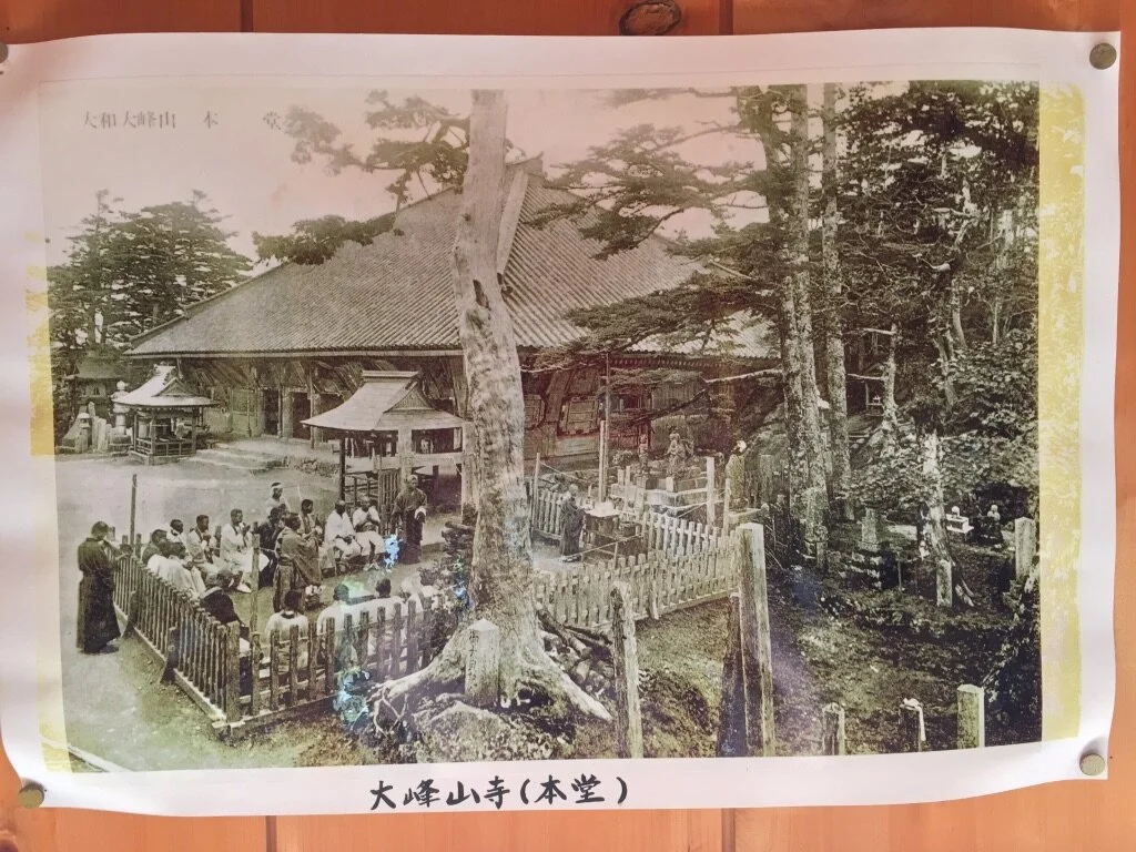 Black and white photo of a group of people gathered outside a traditional Japanese temple with wooden structures and trees.