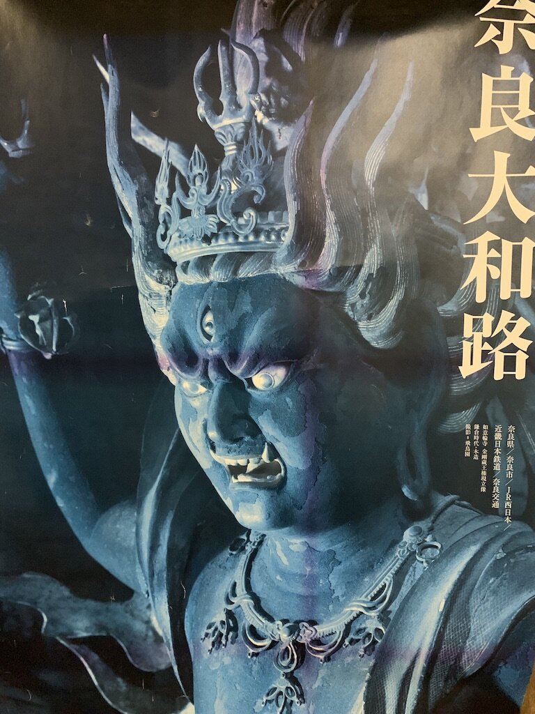 Close-up of a detailed statue of a fierce mythological creature with a crown, featuring blue skin, glowing eyes, and an angry expression, with Japanese text overlay on the right side.