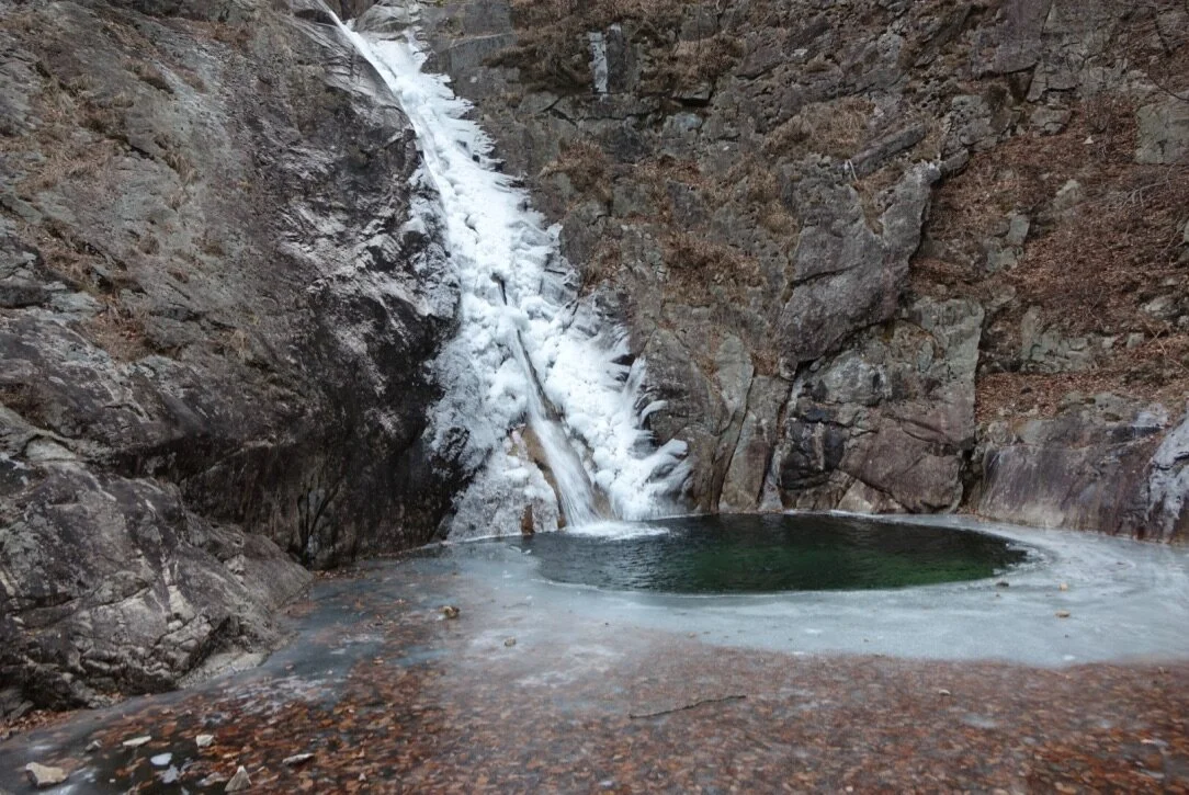 A frozen waterfall cascading into a small pool of water in a rocky canyon.