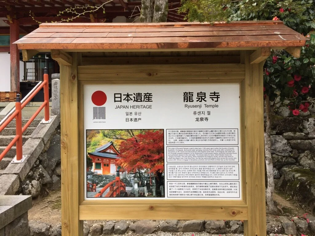 Information board at Ryuzenji Temple displaying Japan Heritage logo, Japanese, Korean, and Chinese text describing the temple, and a photo of the temple with autumn foliage.