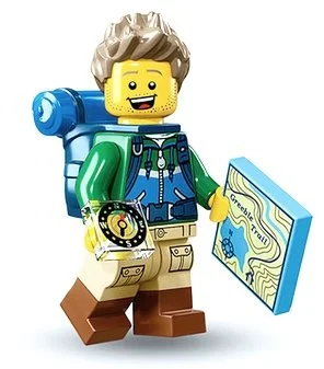 Lego figurine of a young man with blond hair, wearing a green shirt, denim jacket, and tan pants, holding a tablet and wearing a backpack with a rolled-up sleeping mat.