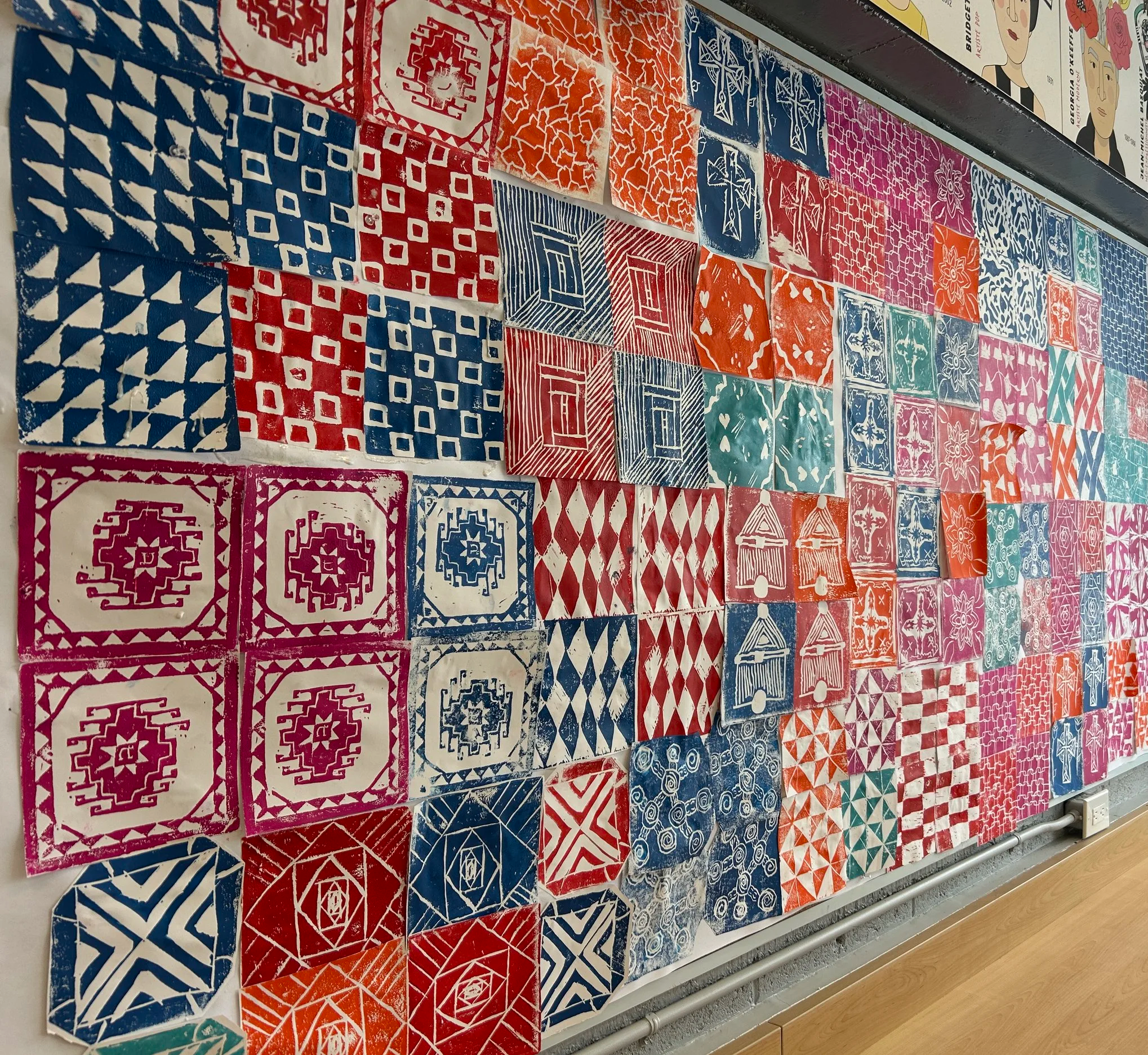 A colorful wall display of various patterned tiles arranged in a grid, featuring geometric and floral designs in red, blue, orange, pink, and green colors.