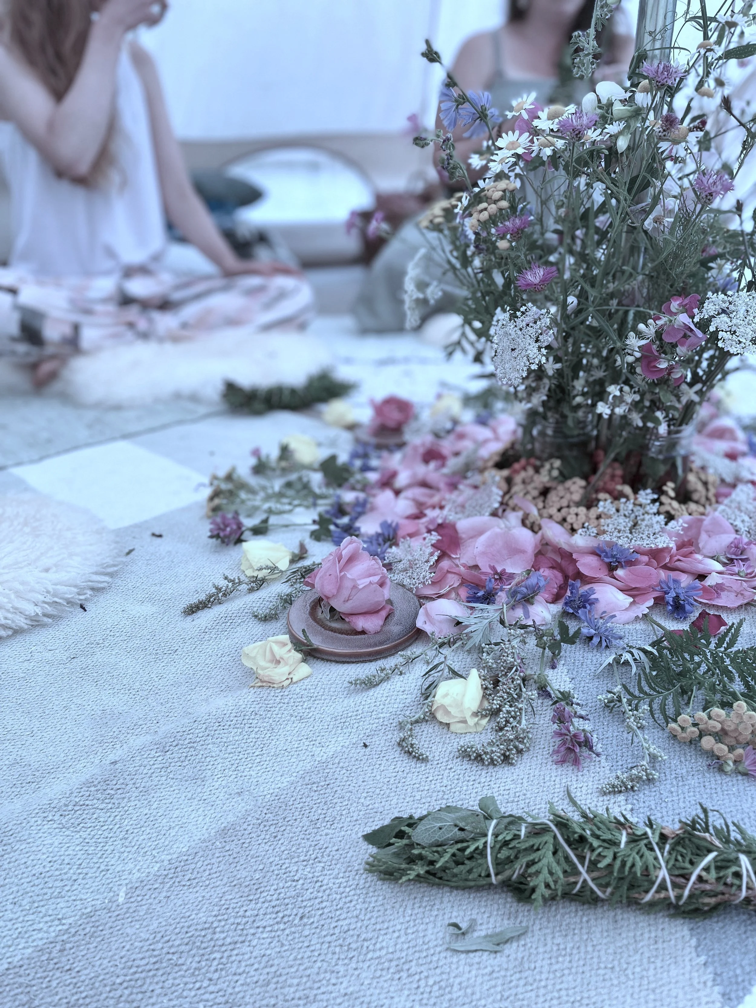 A floral centrepiece on a blanket on the floor surrounded by women seated cross-legged