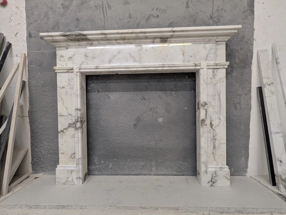 Marble fireplace mantel against a gray wall with some construction materials nearby.