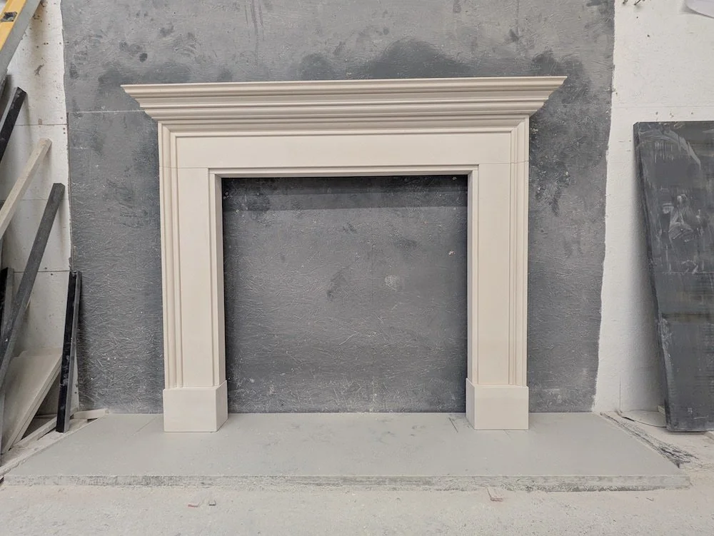 A decorative white fireplace surround with detailed molding, installed on a gray wall in a workshop or warehouse setting.