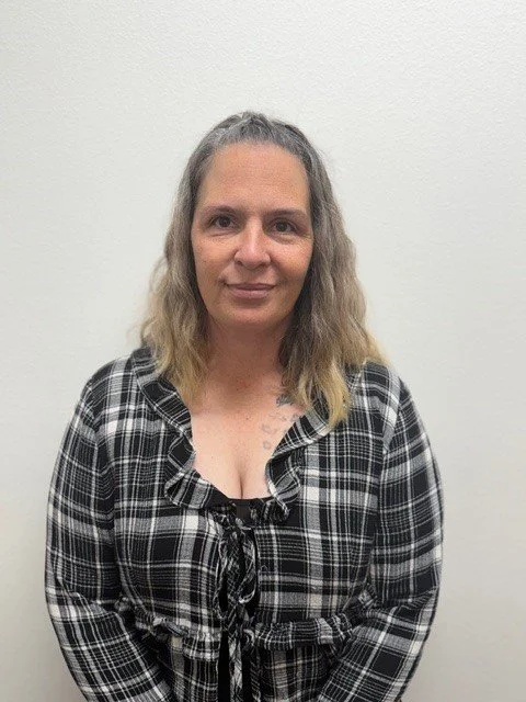 A woman standing in front of a brick wall, wearing a maroon McDonald's uniform shirt with a black long-sleeve shirt underneath, and a blue patterned neck scarf.