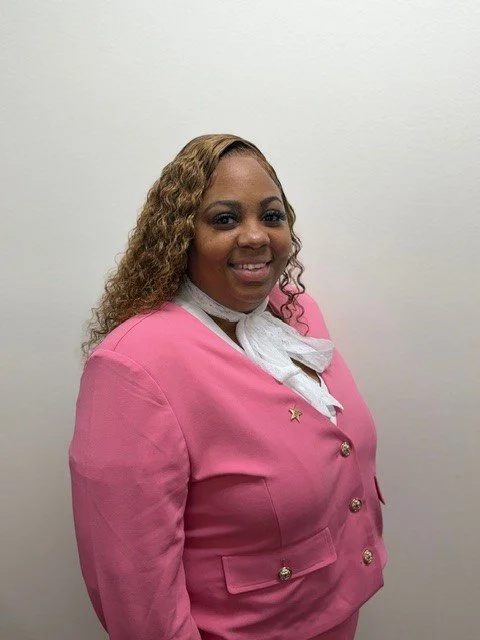 A woman smiling in front of a brick wall, wearing a white shirt and a patterned scarf.
