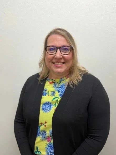 A woman wearing glasses and a McDonald's uniform, standing in front of a brick wall.