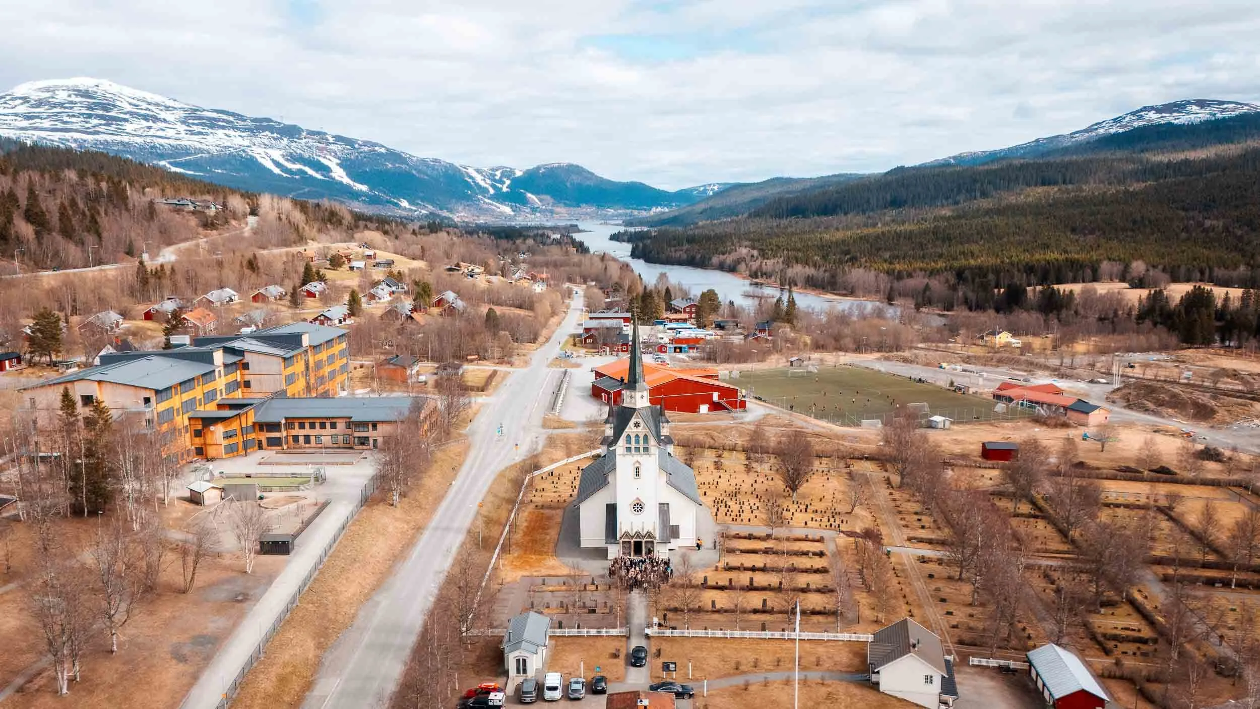 A church wedding in a mountain setting, photographed from the air with guests gathered outside