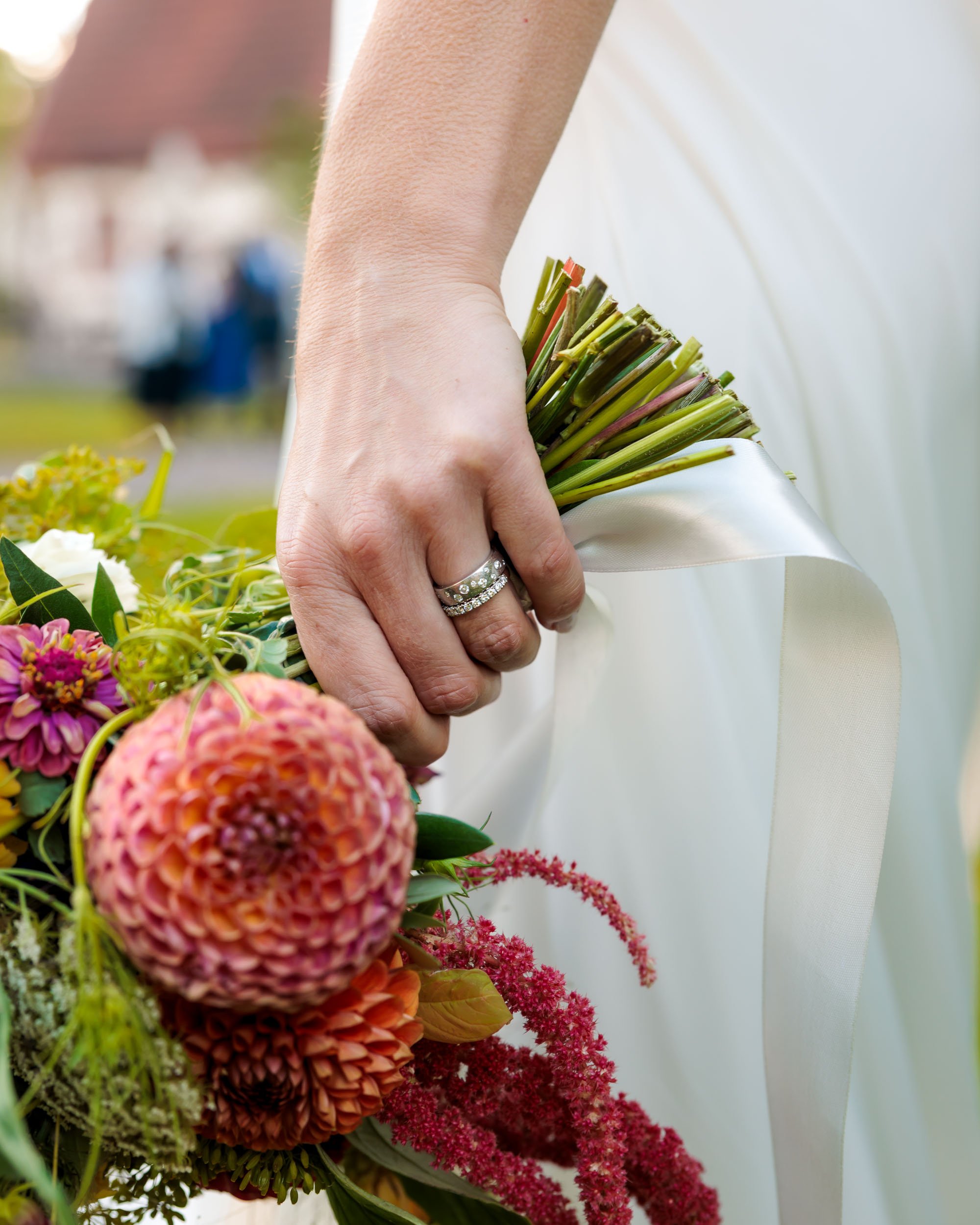 En hand med vigselring håller en bunt blommor på ett bröllop.