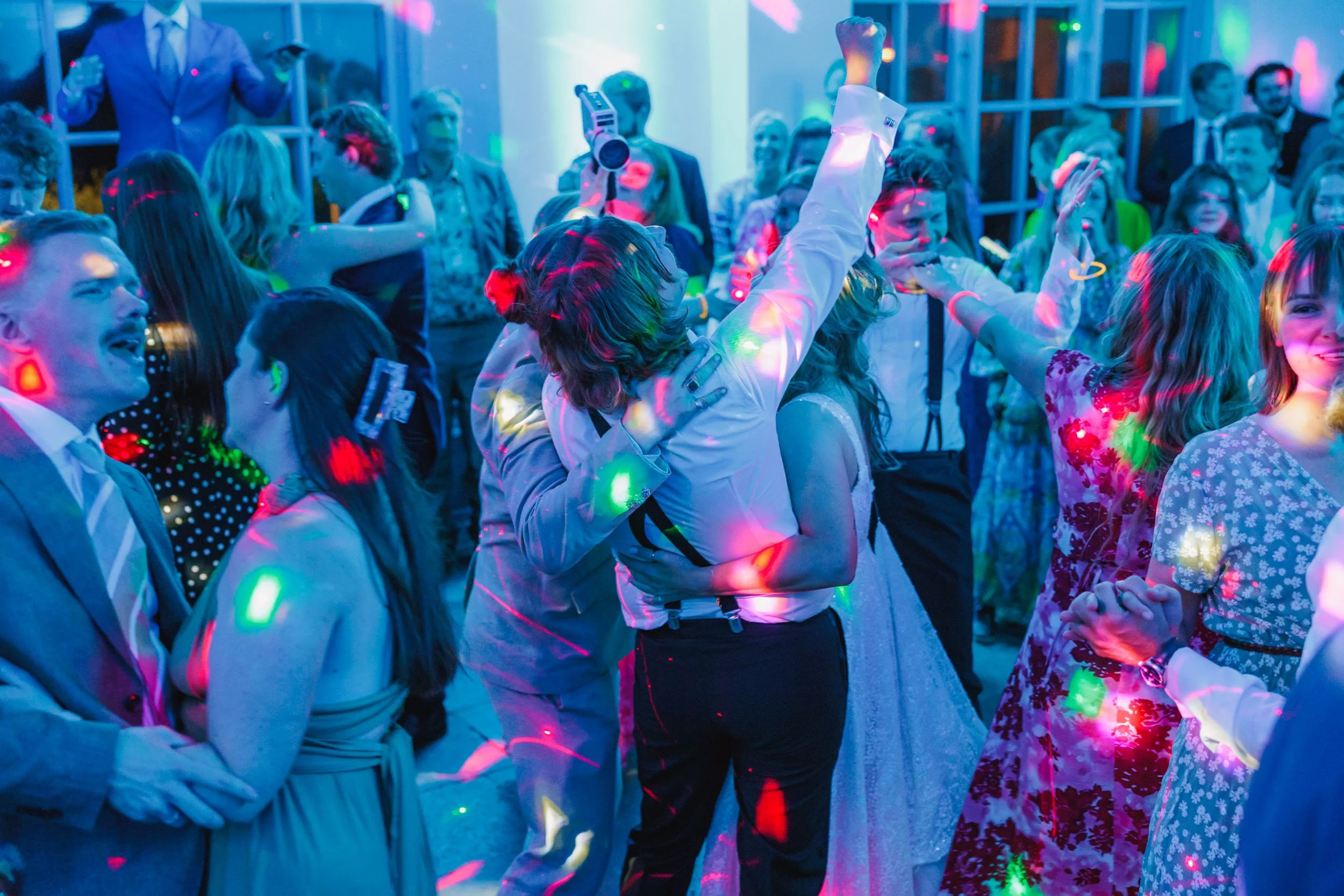 Mänskor dansar på ett festmoment, med färgglada disco-ljus, i en festlokal. Några är gifta och pratar, medan andra dansar tillsammans.