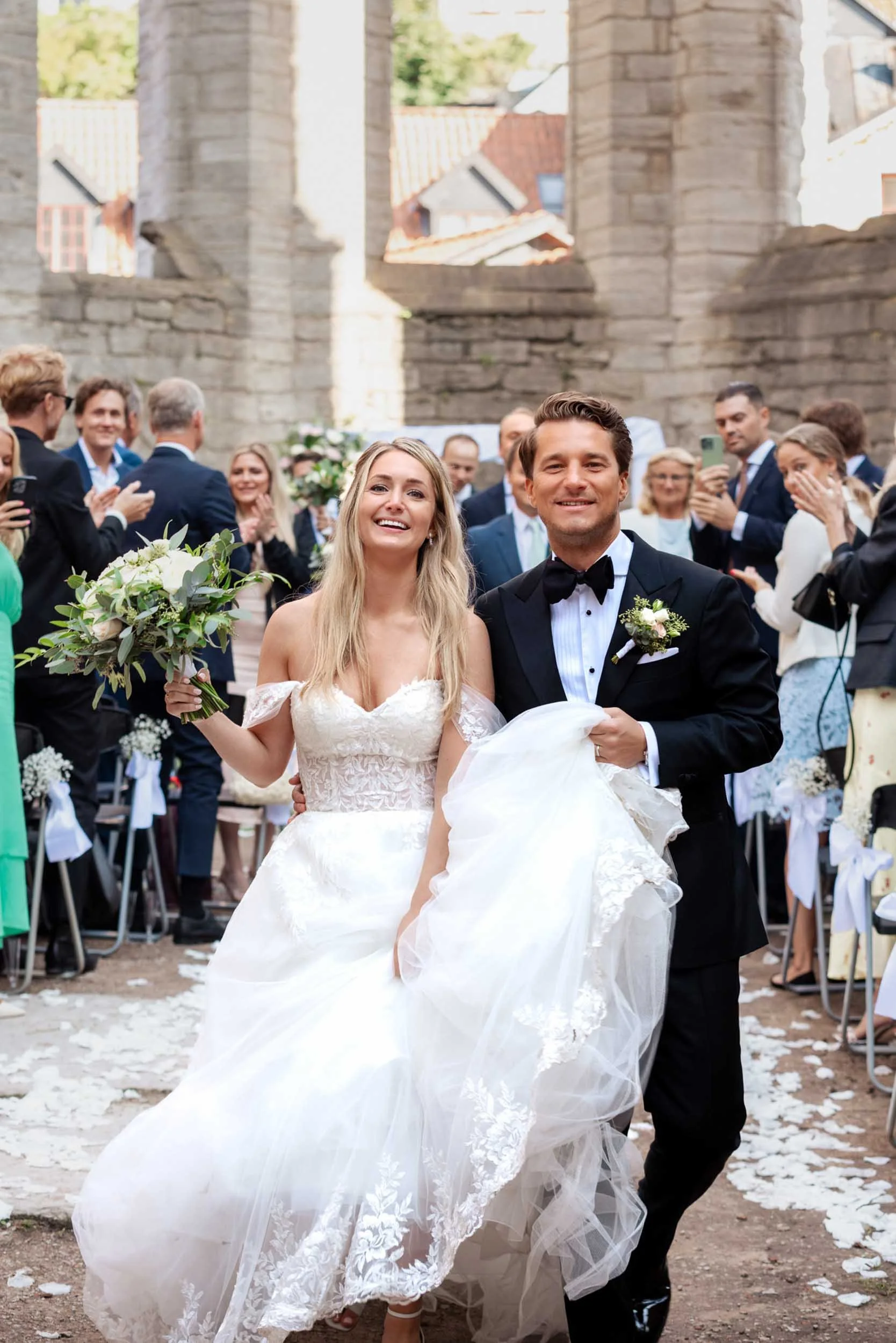 Nyligen gifta par som går ut ur en kyrka, omgivna av glada gäster, med blommor och förälskelse i luften.