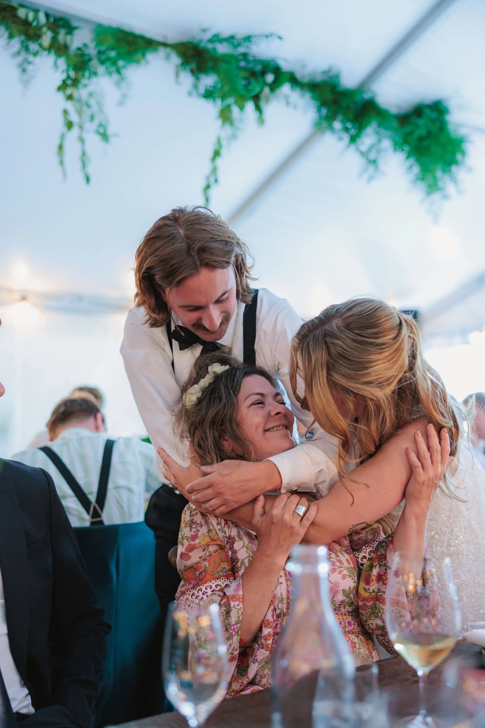 Glada människor som omfamnar varandra vid ett festligt tillfälle under en tältfest, dekorerat med gröna växter.