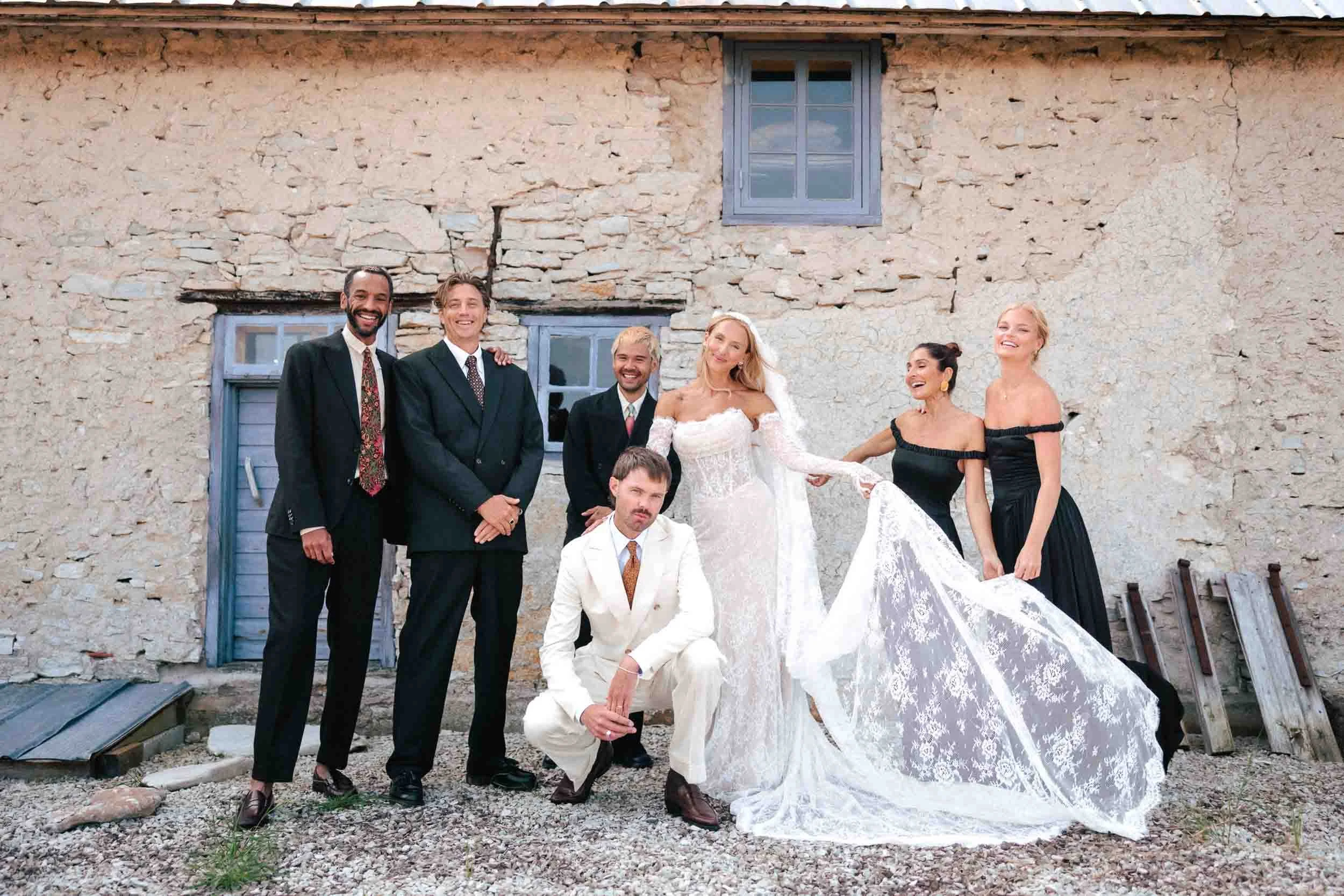 Bröllopspar med brudgummar och tärnor vid stenmur – gruppfoto bröllop Sverige
