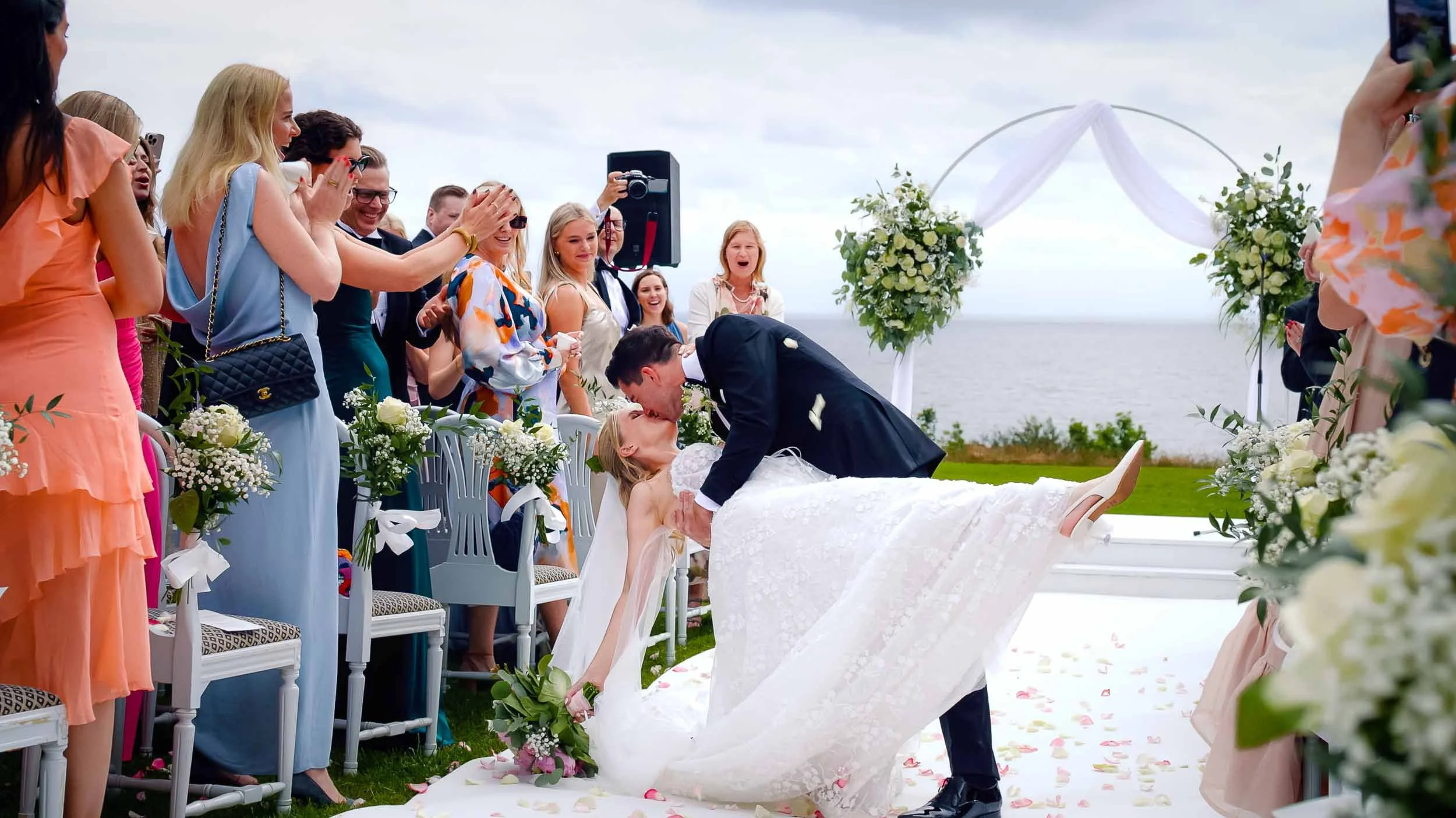 A bride and groom kiss after their outdoor wedding by the sea; a joyful moment captured in a wedding photo