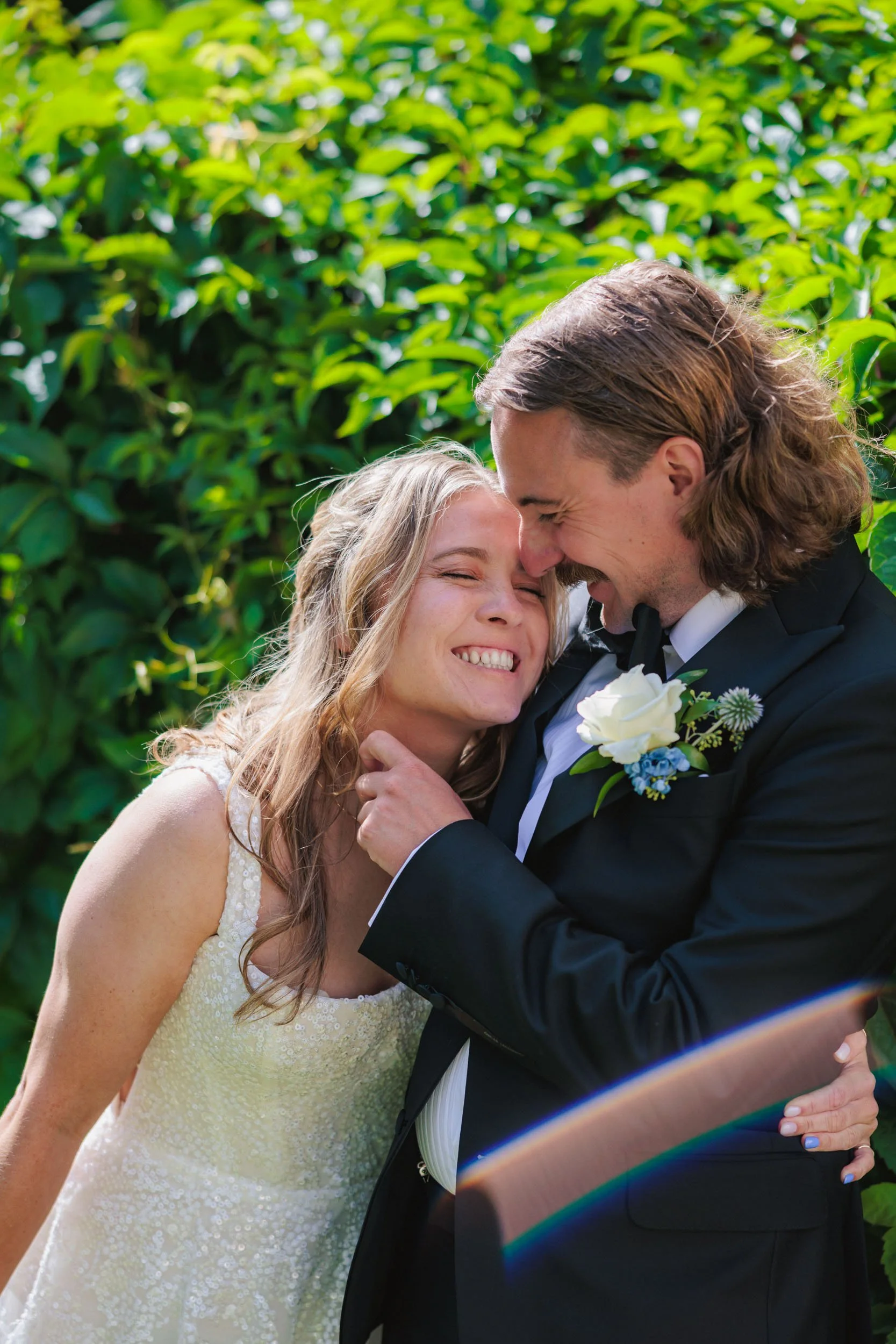 En glad brud och brudgum kramas och ler inför en grön bakgrund.