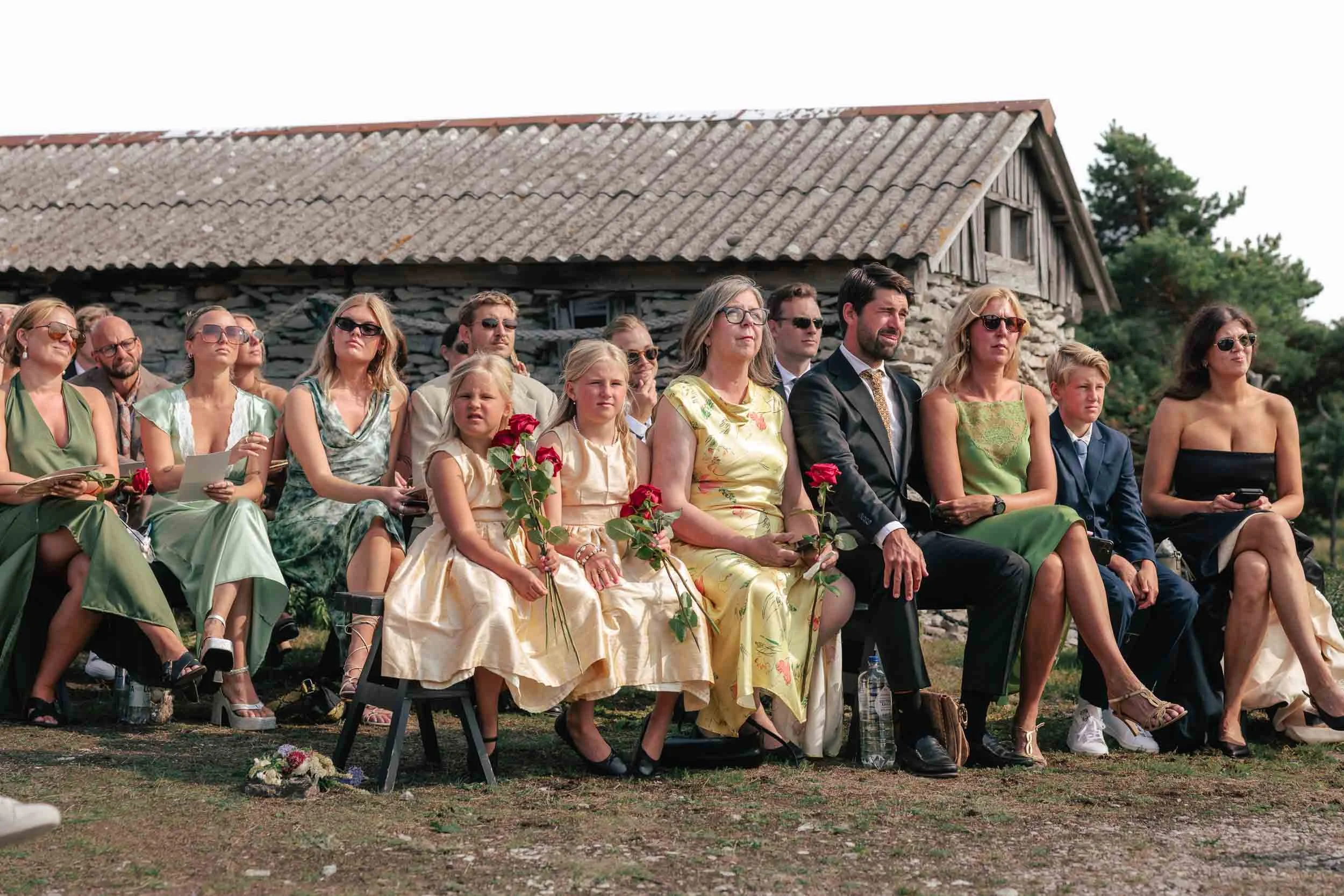 Wedding guests gathered during an outdoor ceremony in a rural setting; documentary photo from the wedding day