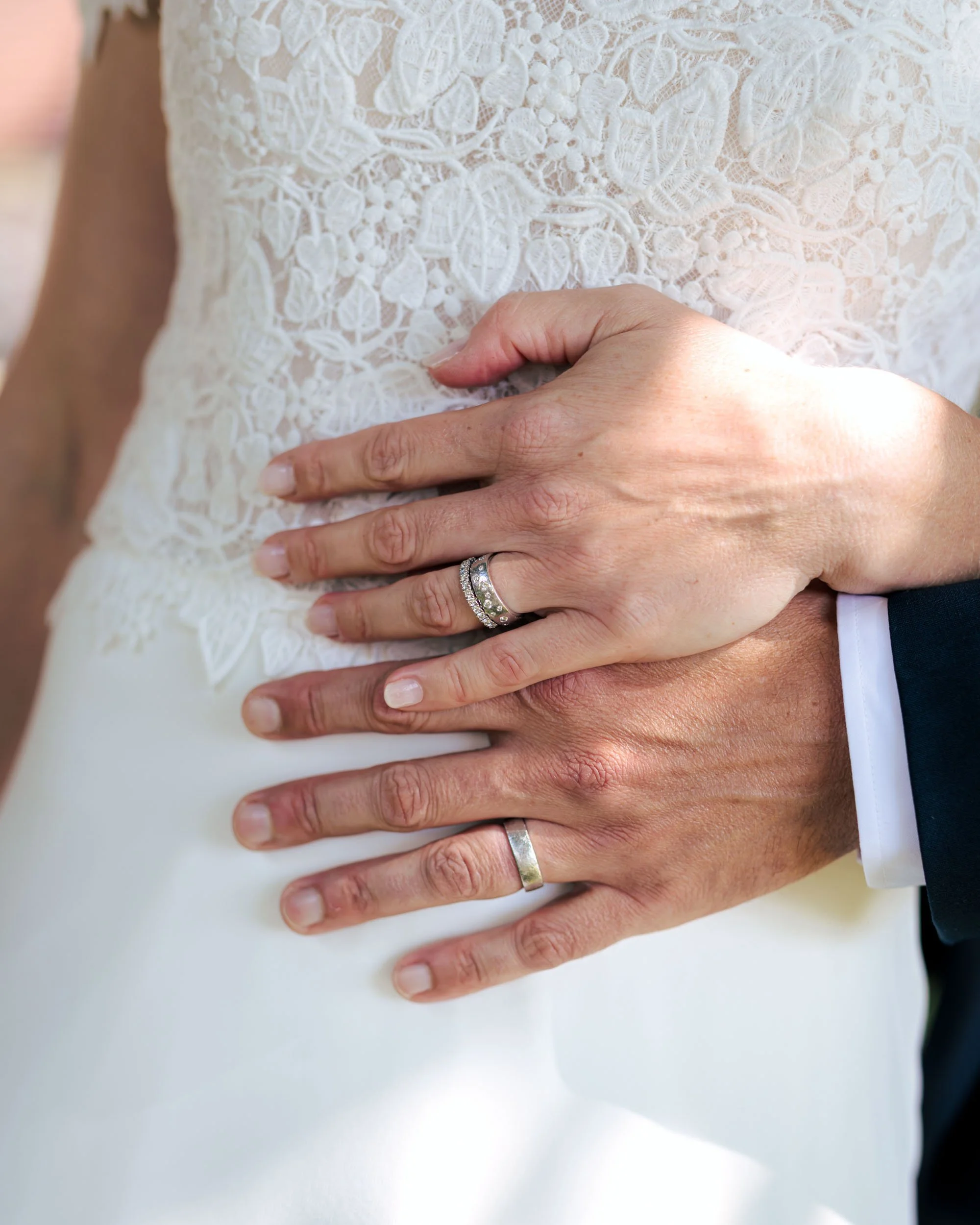 Två personer håller varandra med händerna på en klänning, båda bär vigselringar.