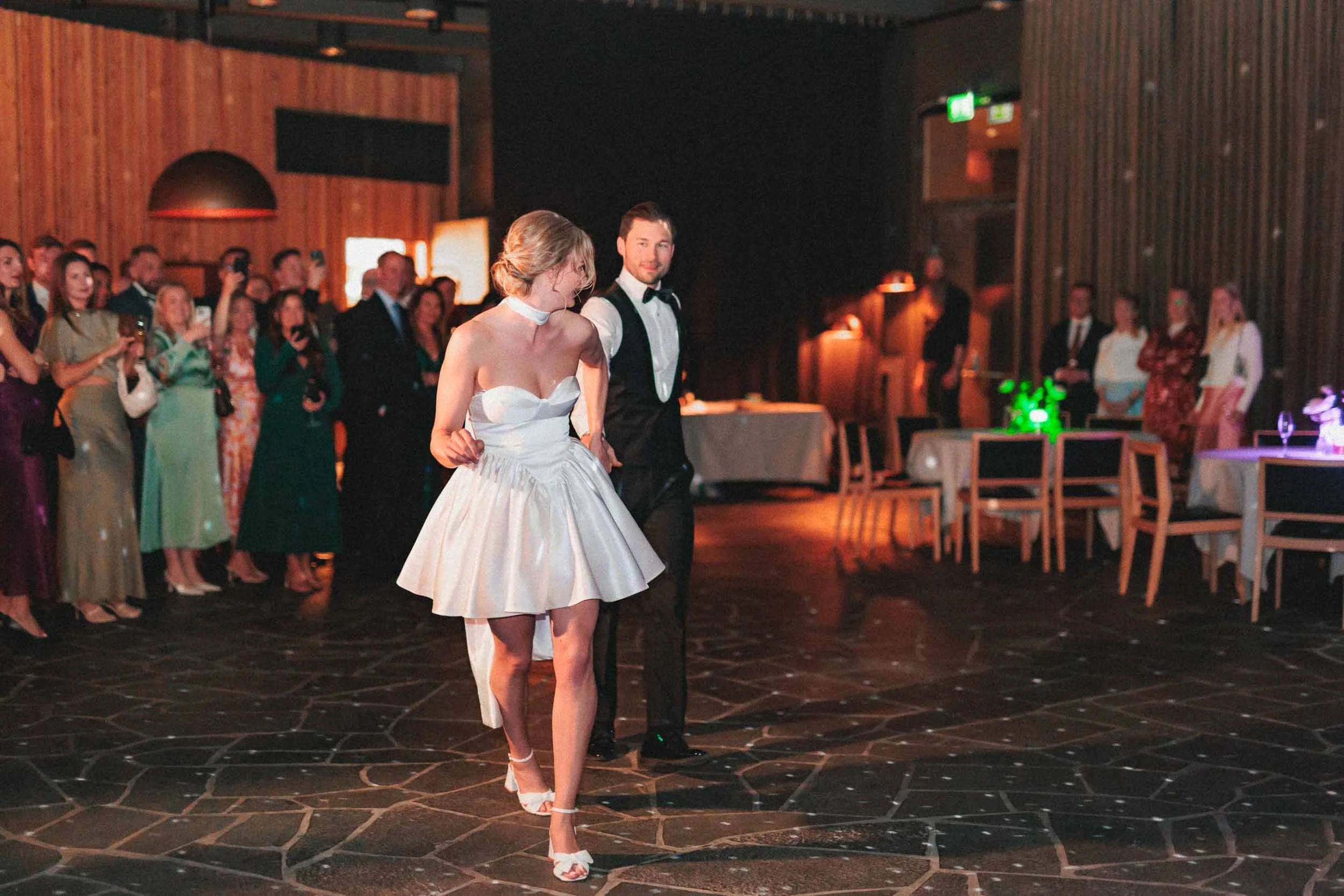 A bride and groom are dancing together in a banquet hall while many guests watch.