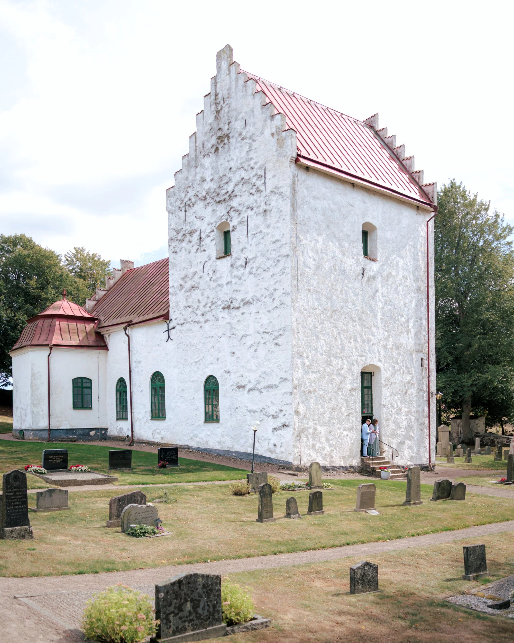 En vit kyrka med röd takplåt omgiven av gravkupor på en kyrkogård.