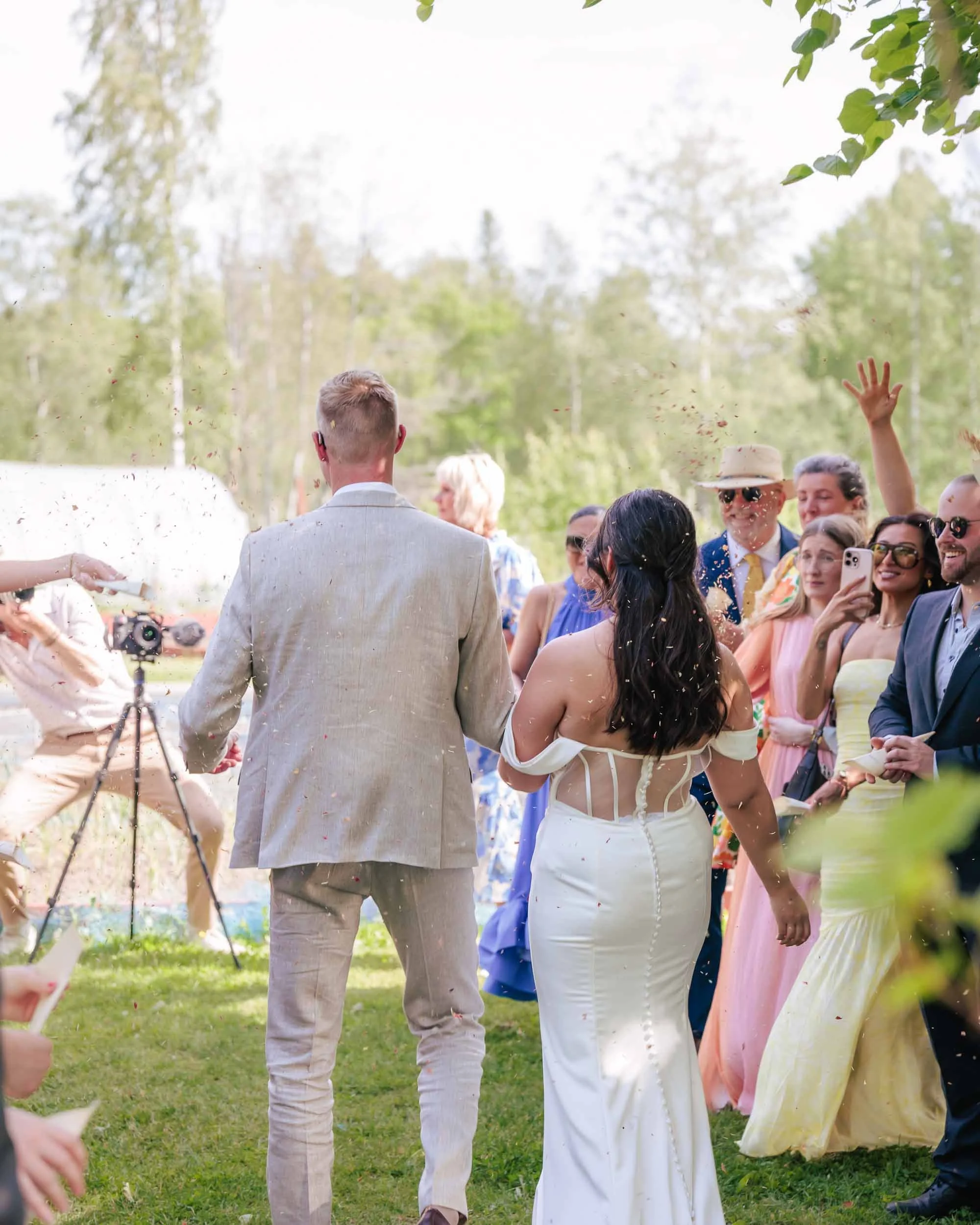 Brudpar sett bakifrån som går genom ett regn av konfetti utomhus; beskrivning av premiumpaketet där både fotograf och videograf dokumenterar hela bröllopsdagen.