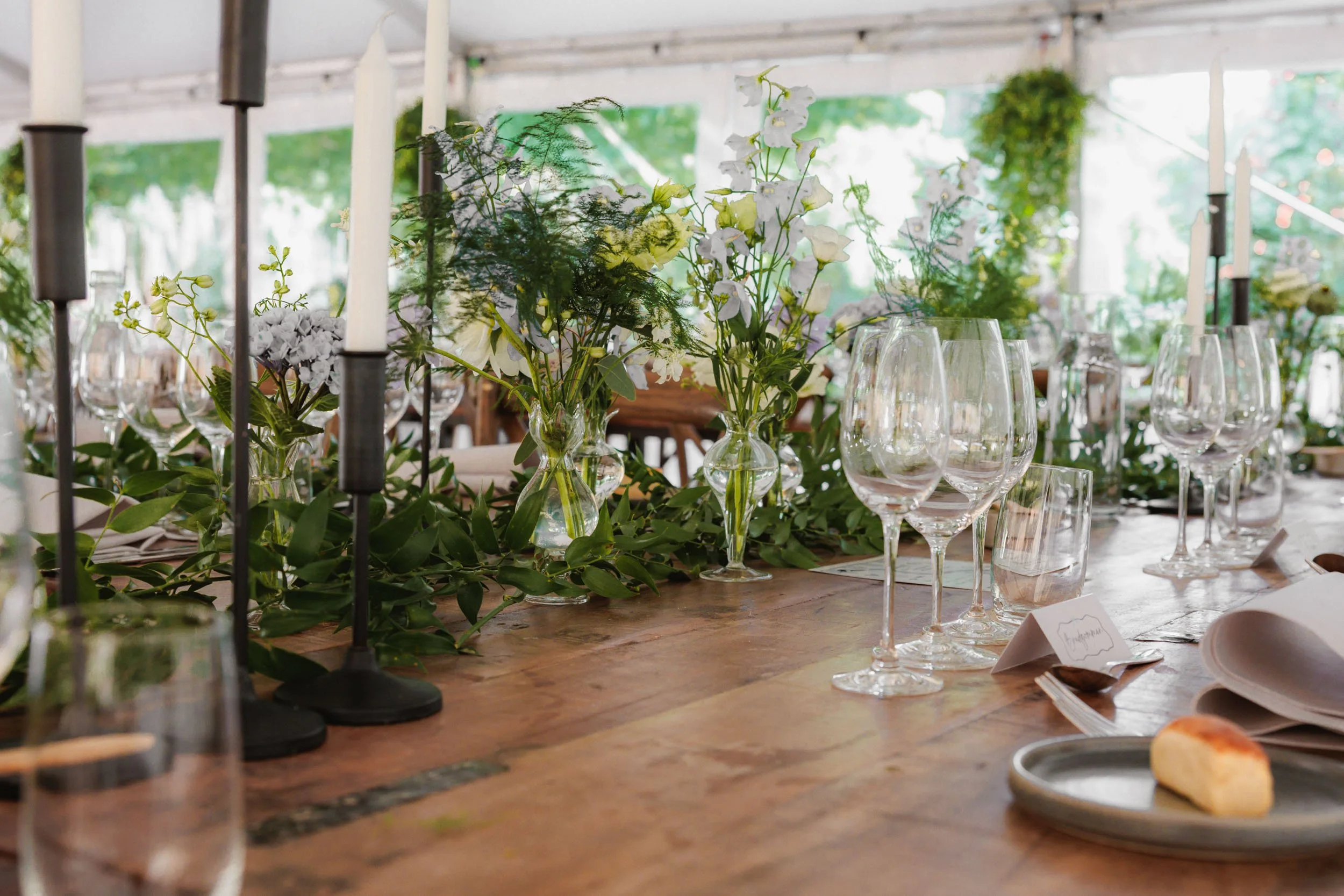 En festmåltidsbord med blomsterarrangemang, tomma vattenglas och ljusstakar på ett träbord.