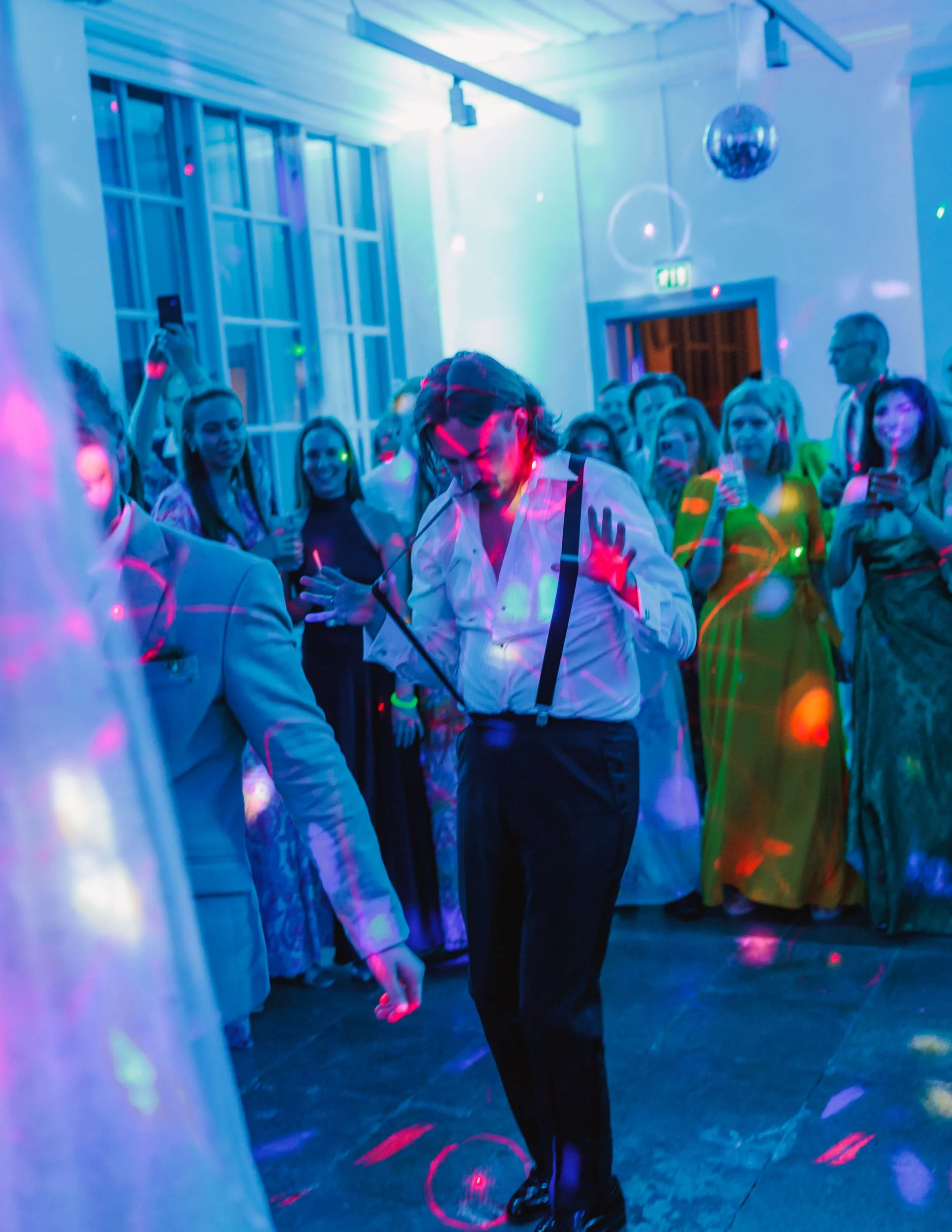 Person dansar på ett dansgolv med fler människor i bakgrunden, färgade ljus och discokula i ett festligt inomhusrum.