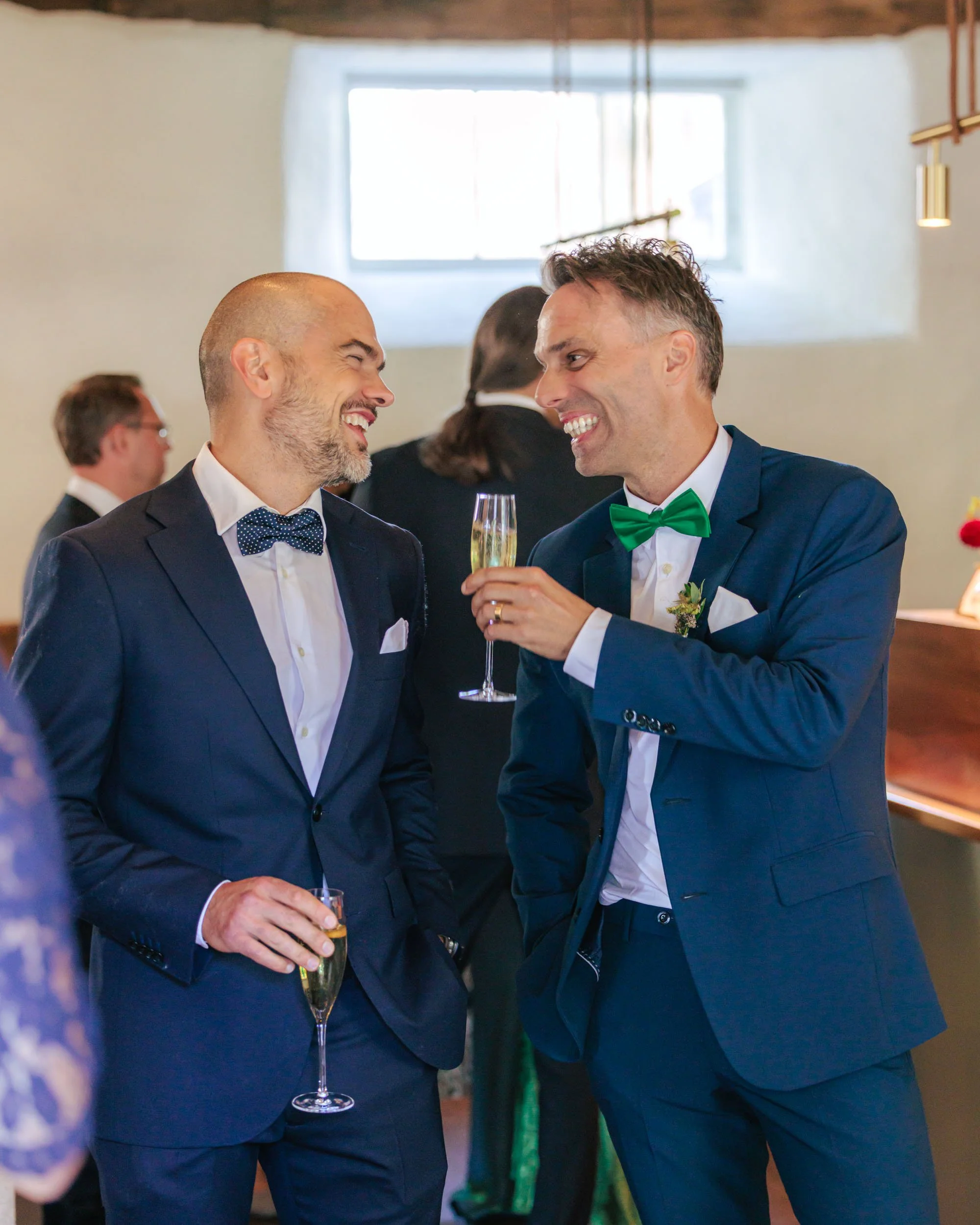 Två män i kostym och fluga som samtalar och skålar vid ett festligt tillfälle.