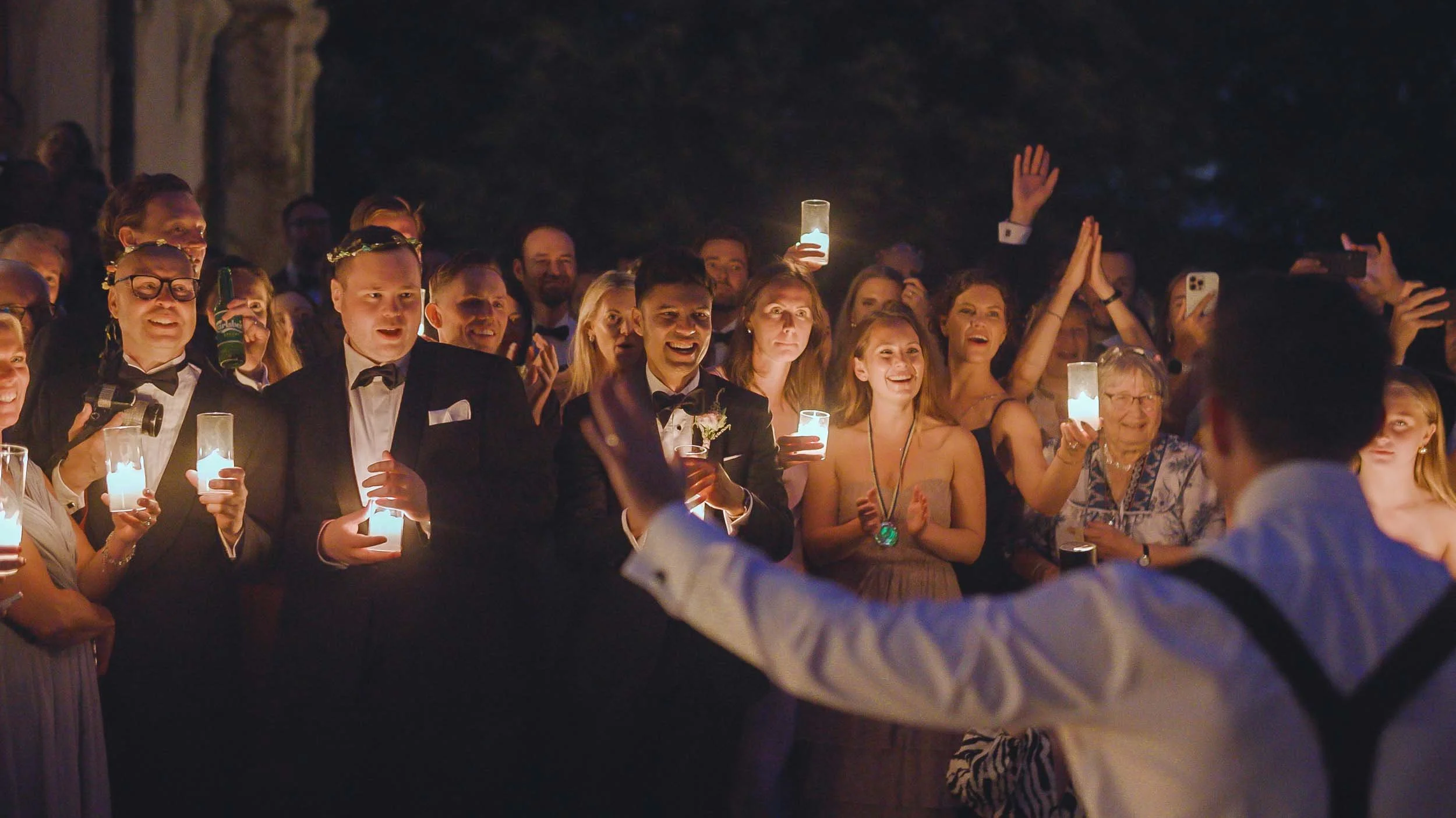 Wedding guests hold candles during the evening celebration and outdoor speeches