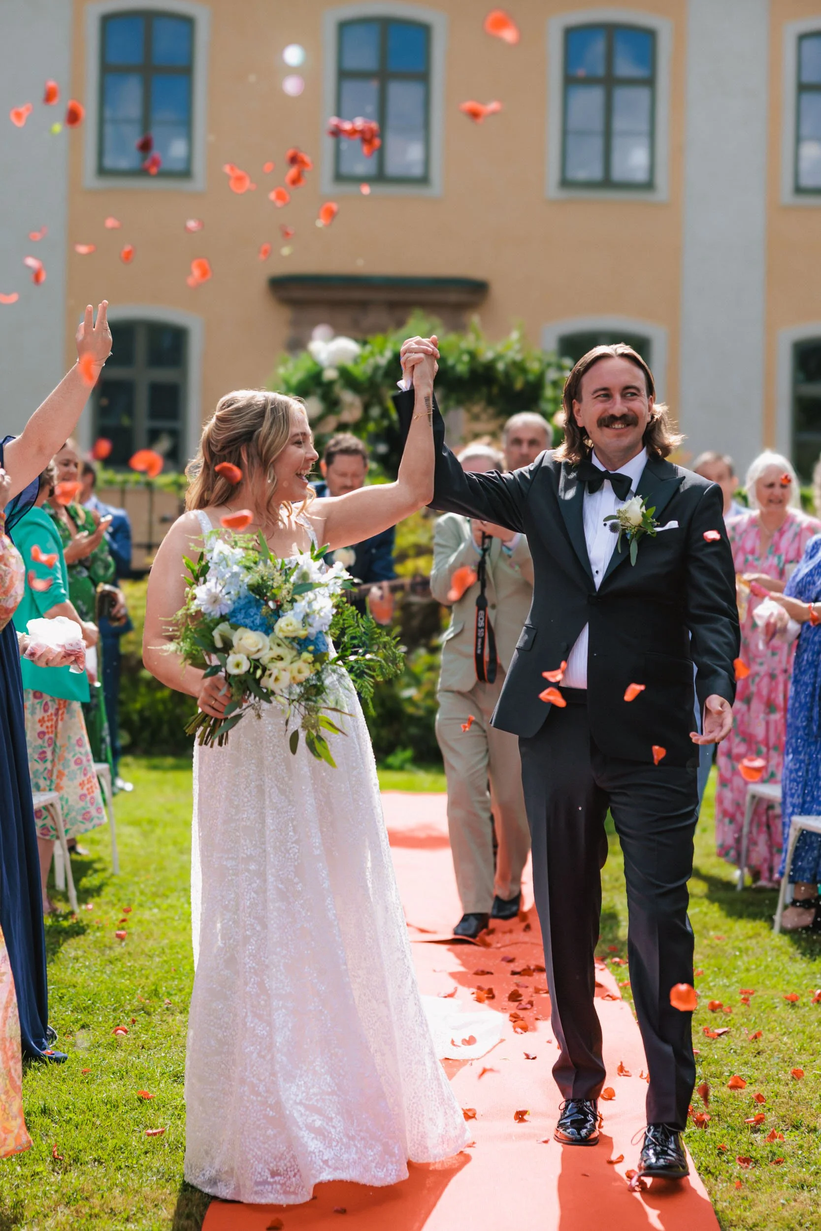 Nytt gifta par som dansar på en utomhusbröllopsfest, omgivna av gäster som kastar blomblad.