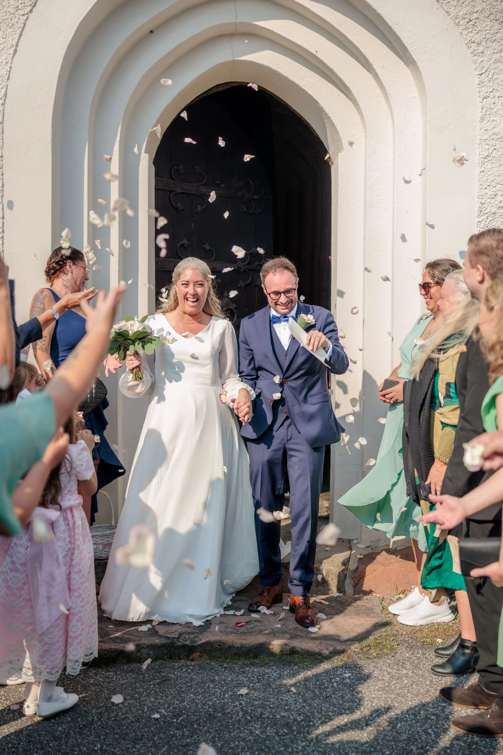 Nykopplade bröllopsparet går ut ur en kyrka medan gäster kastar blomblad.