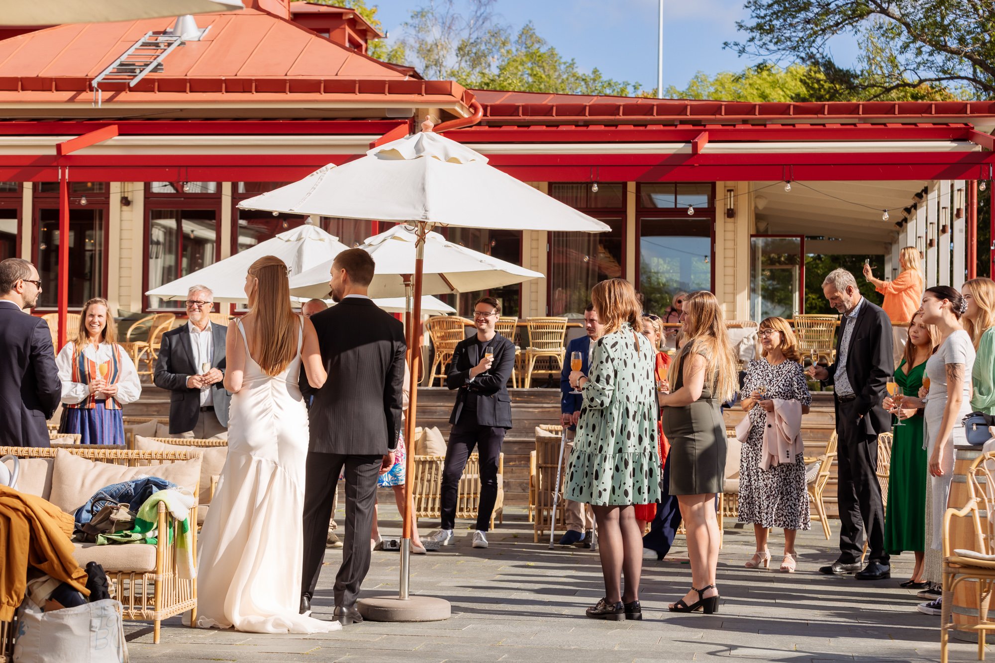 Bröllopspar minglar med gäster på solig restaurangterrass – litet bröllop Sverige