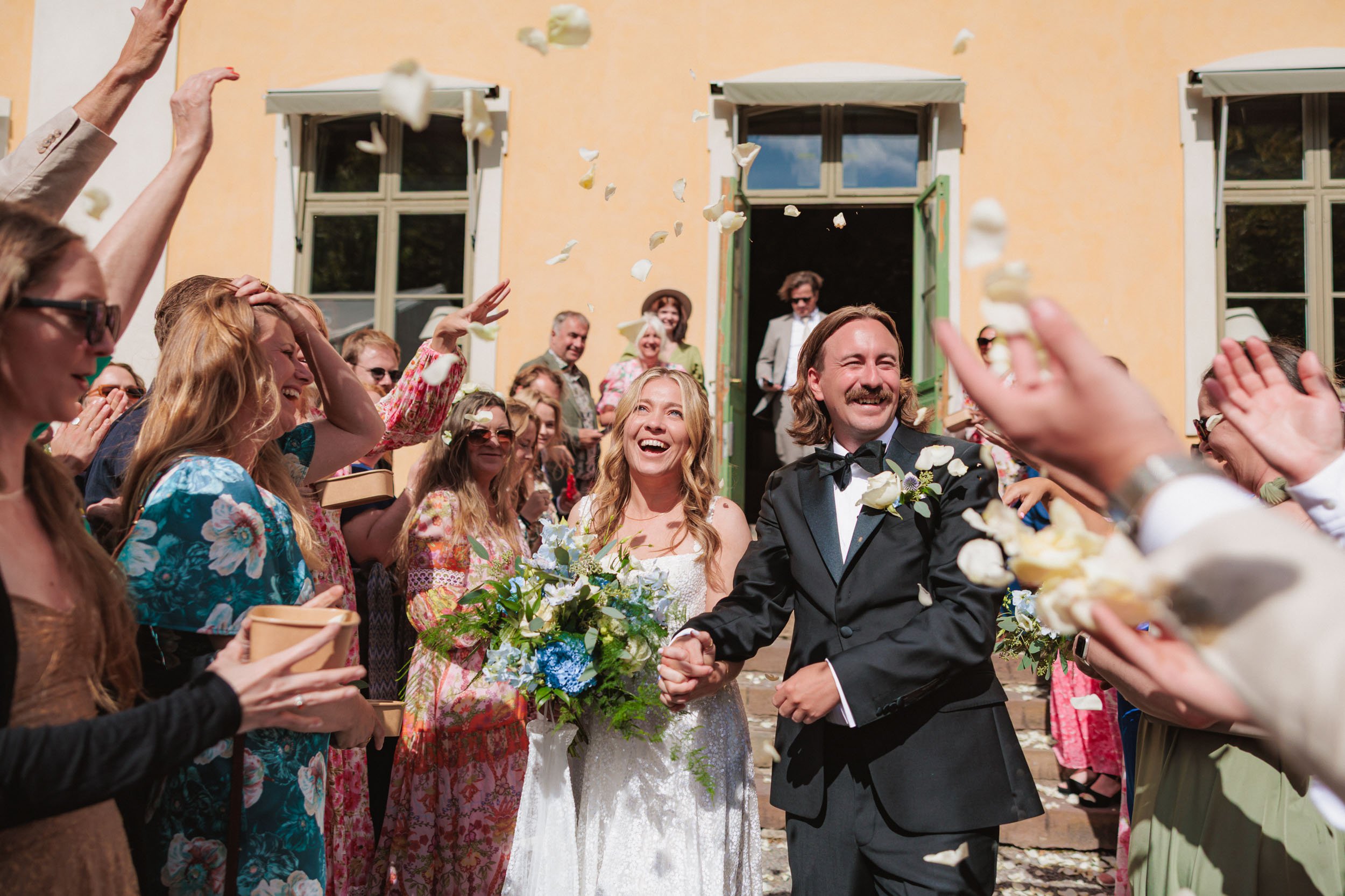 jublande brudpar som lämnar sin vigsel i ett blomregn.