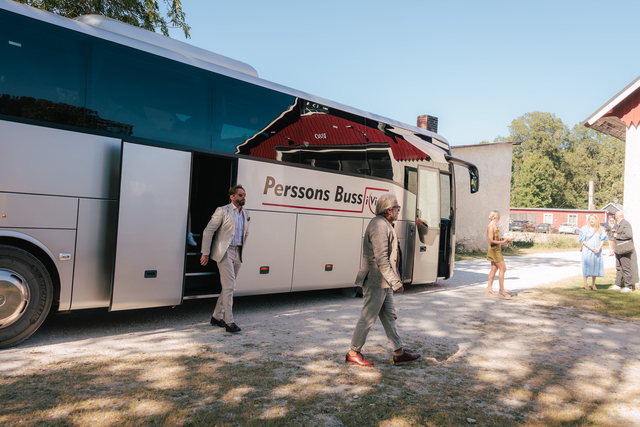 Bröllopsklädda gäster kliver av gemensam charterbuss vid bröllopsvenue på sommaren