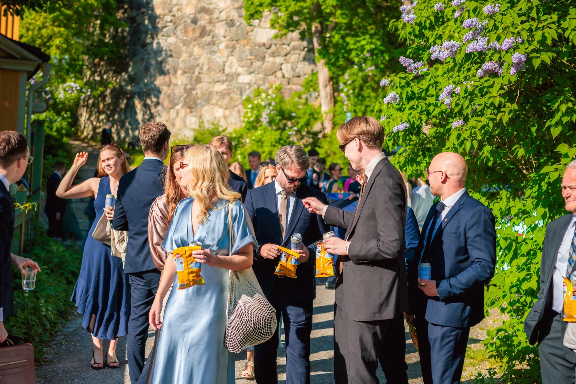 Bröllopsgäster minglar utomhus i solen med lila syrener – bröllop Stockholm sommar