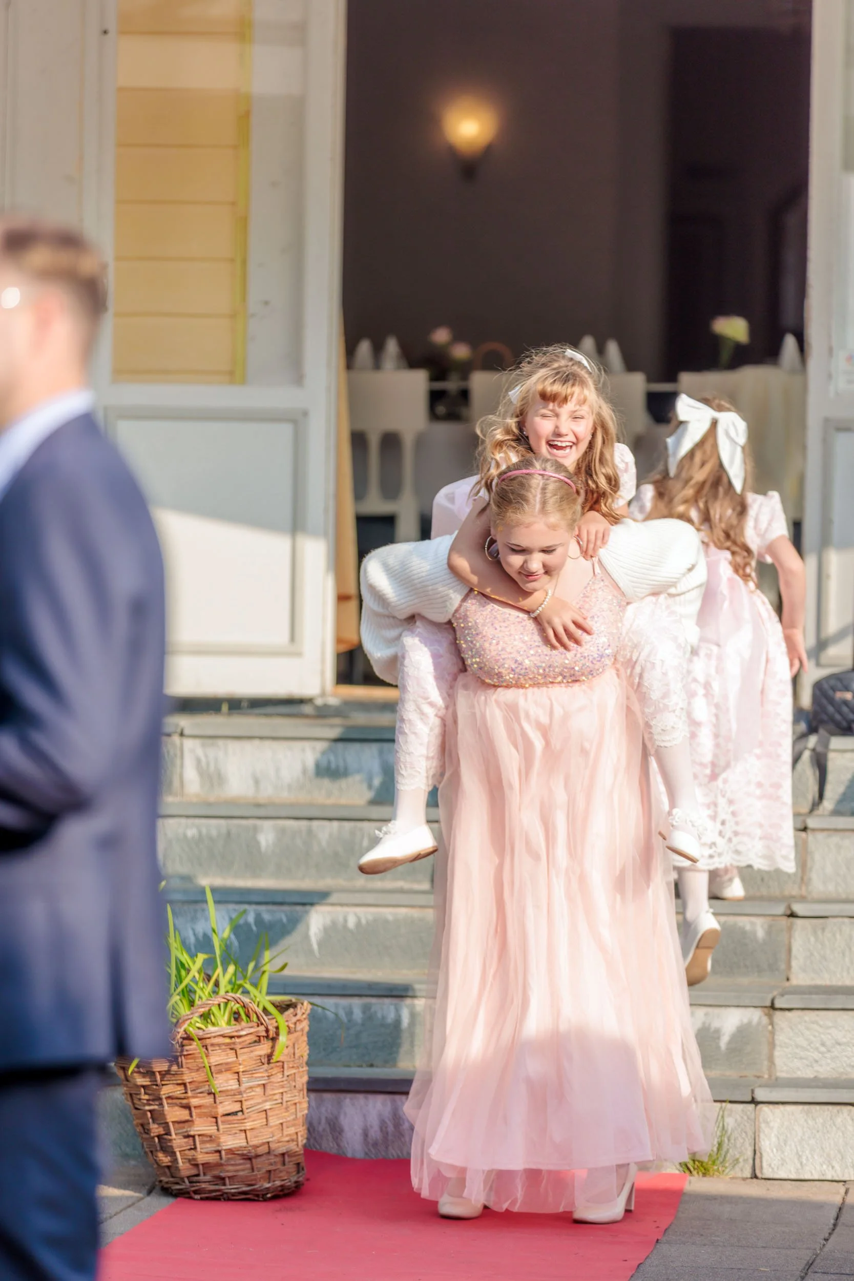 Barn som leker och har roligt utomhus, en flicka får en annan att rida på ryggen, alla är klädda i festkläder.