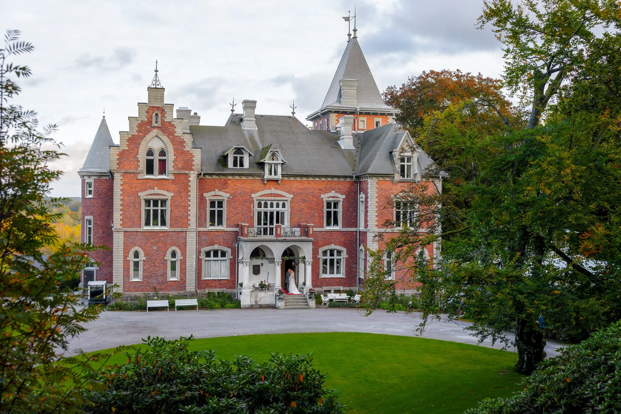 Bröllopspar i entrén till rött tegelslott omgivet av höstlöv – bröllopslokal slott Sverige