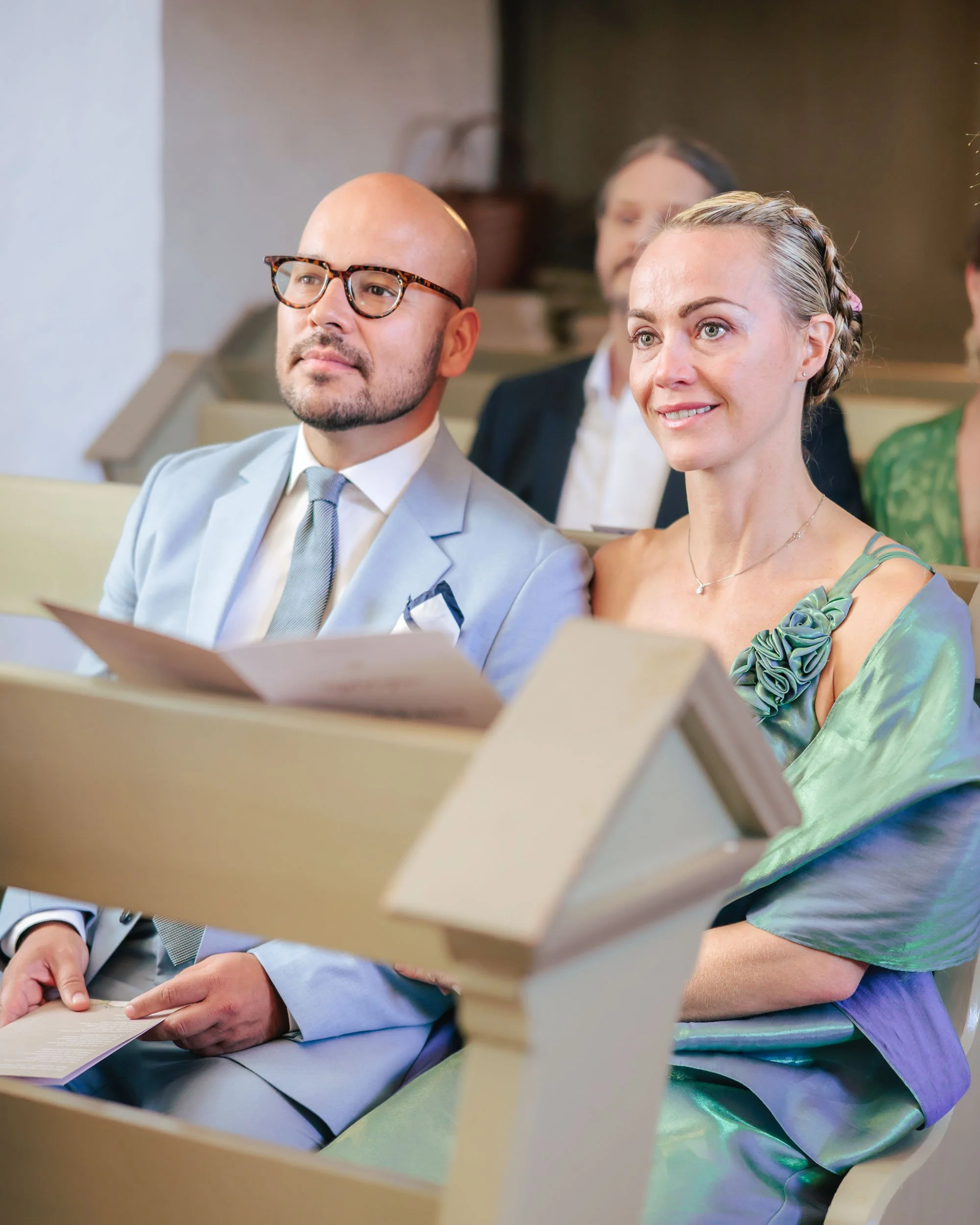 Människor sitter i ett kyrkbänk under en ceremoni, troligen ett bröllop, i en kyrka.