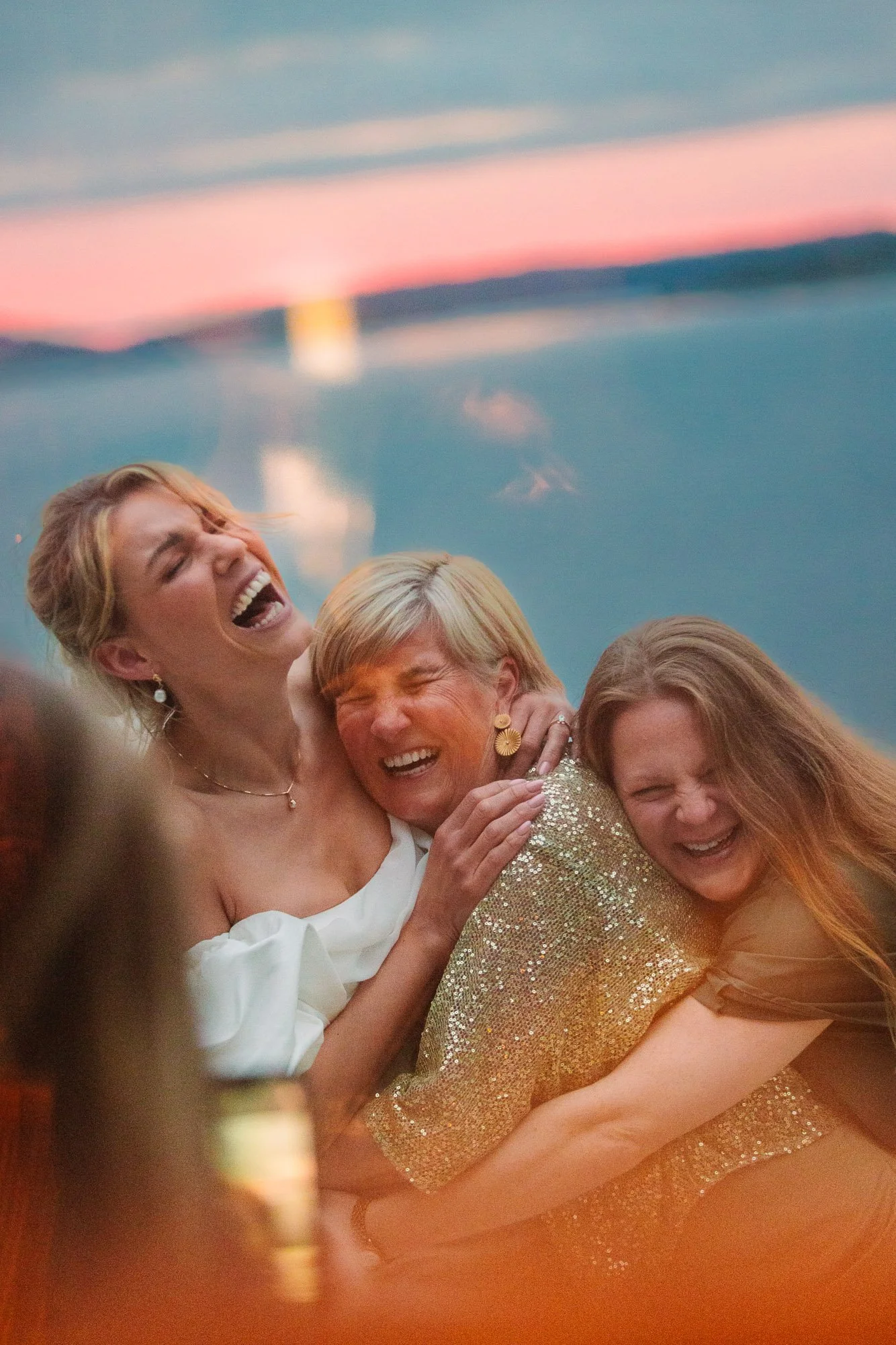 Brud skrattar tillsammans med två kvinnliga släktingar i varmt kvällsljus utomhus