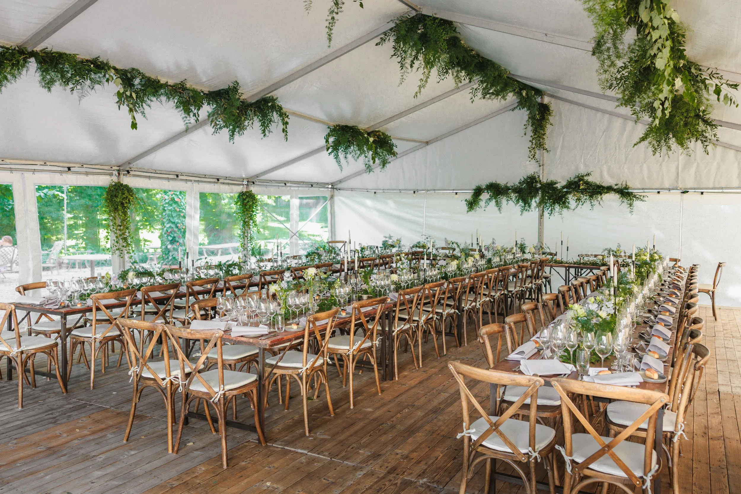 Ett festtält med dukade långbord, bordsdekorationer med gröna växter och vita blommor, förberedelser inför ett evenemang.